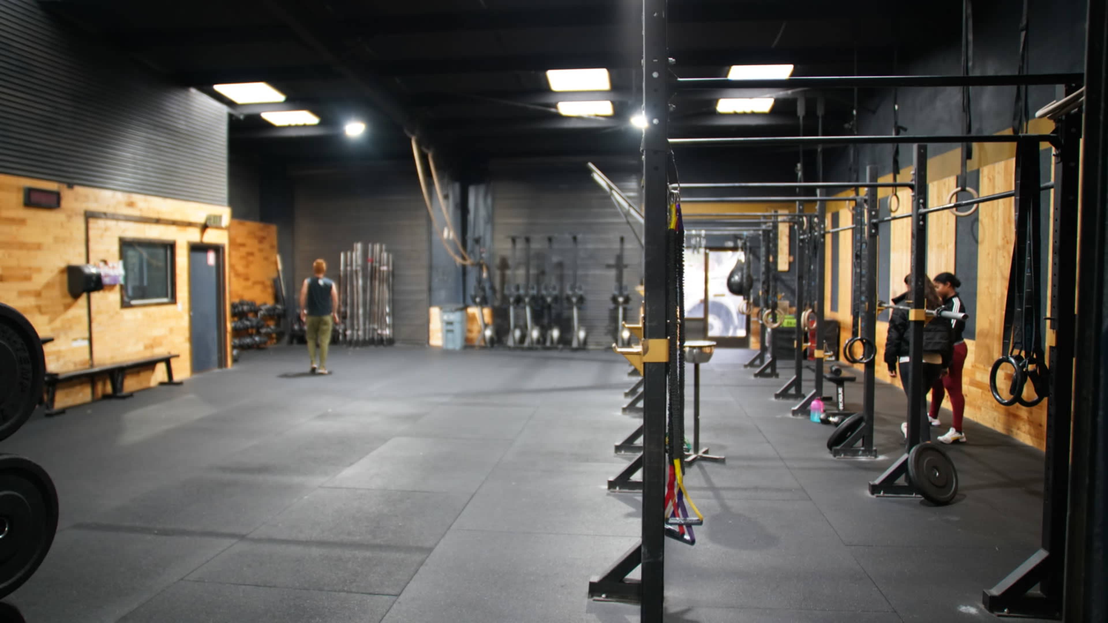 A spacious gym interior with various workout equipment, including weightlifting bars and gymnastic rings arranged on both sides of the room.