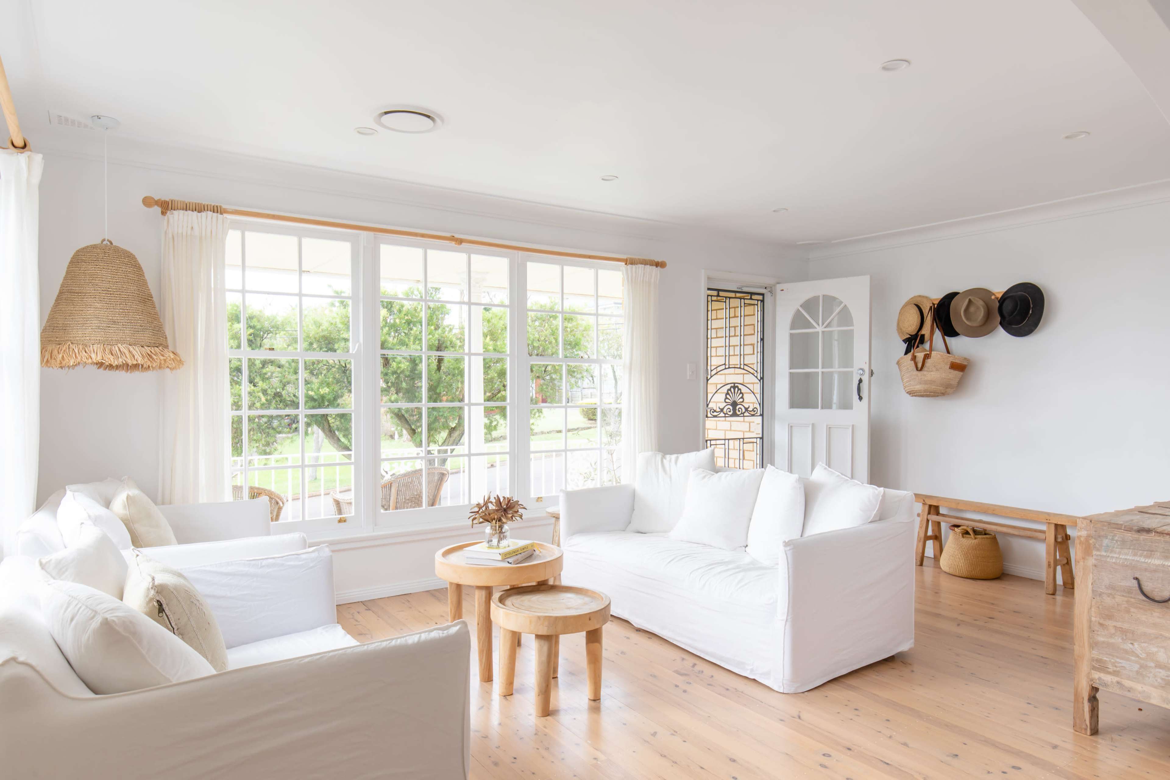 A bright, airy living room with white sofas, wooden accents, and large windows allowing natural light to fill the space.
