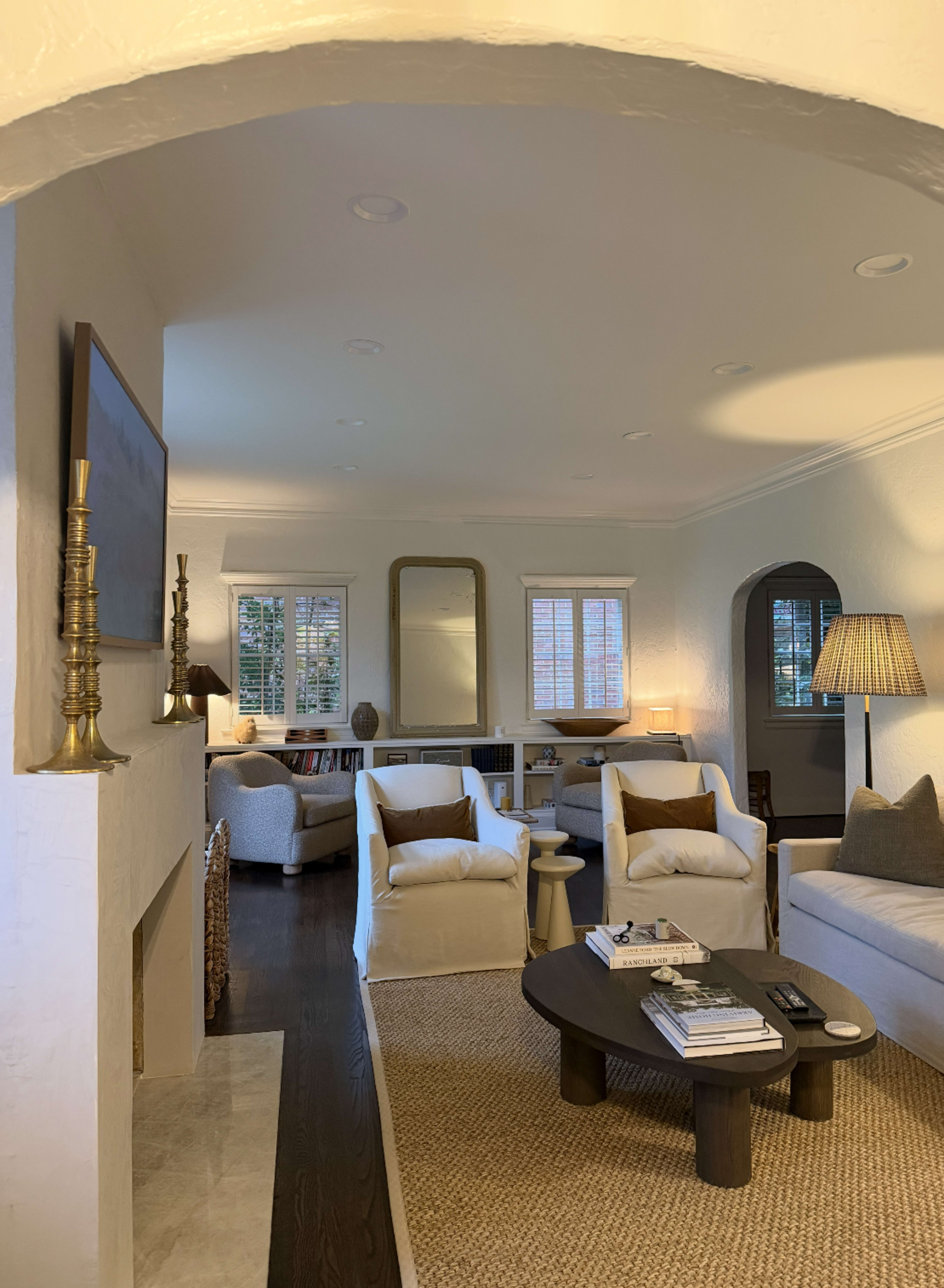The image shows a cozy living room with white walls, comfortable seating, a coffee table, and a fireplace, illuminated by warm lighting.