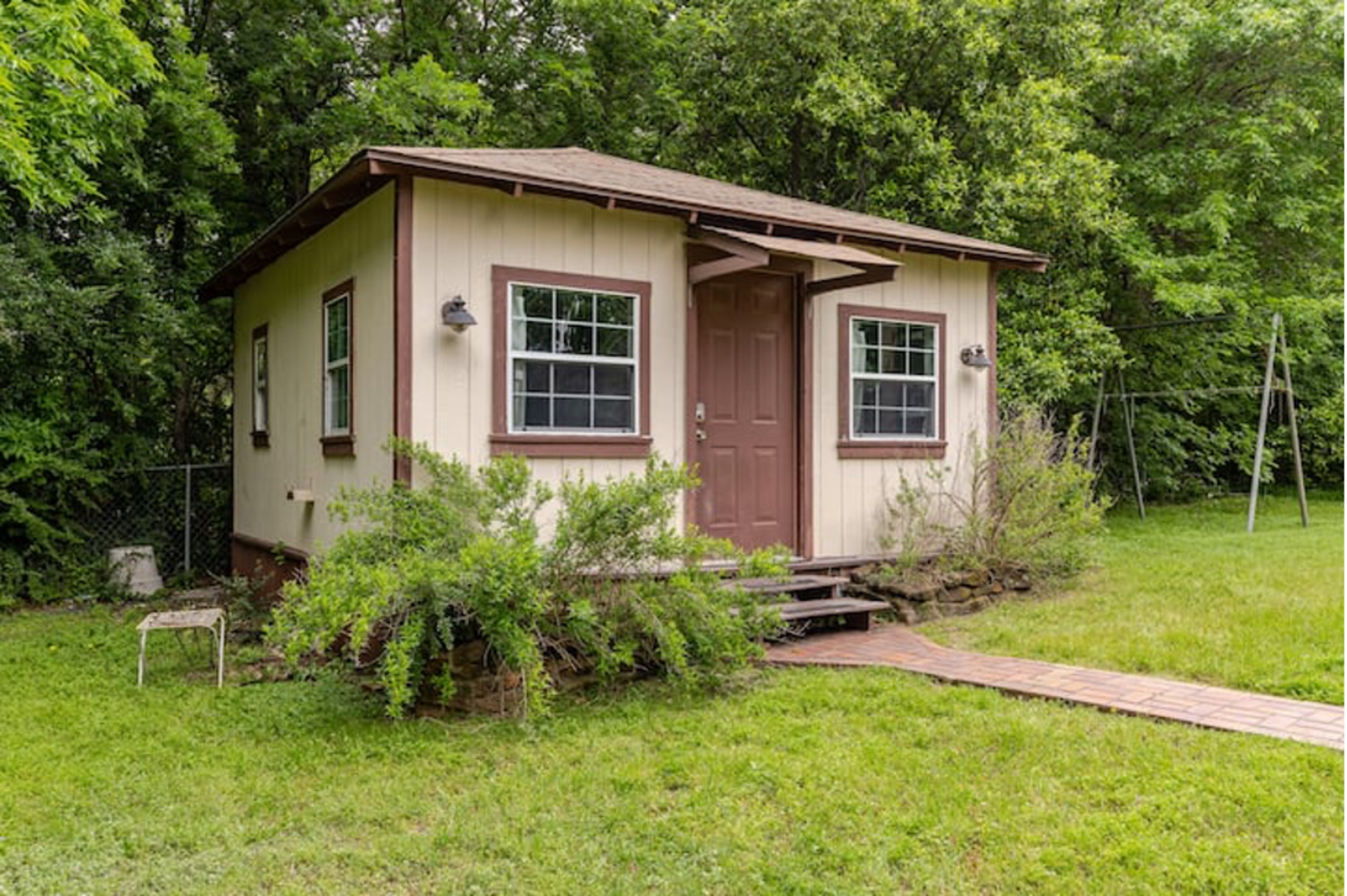 A small, single-story building with a porch sits surrounded by grass and trees.