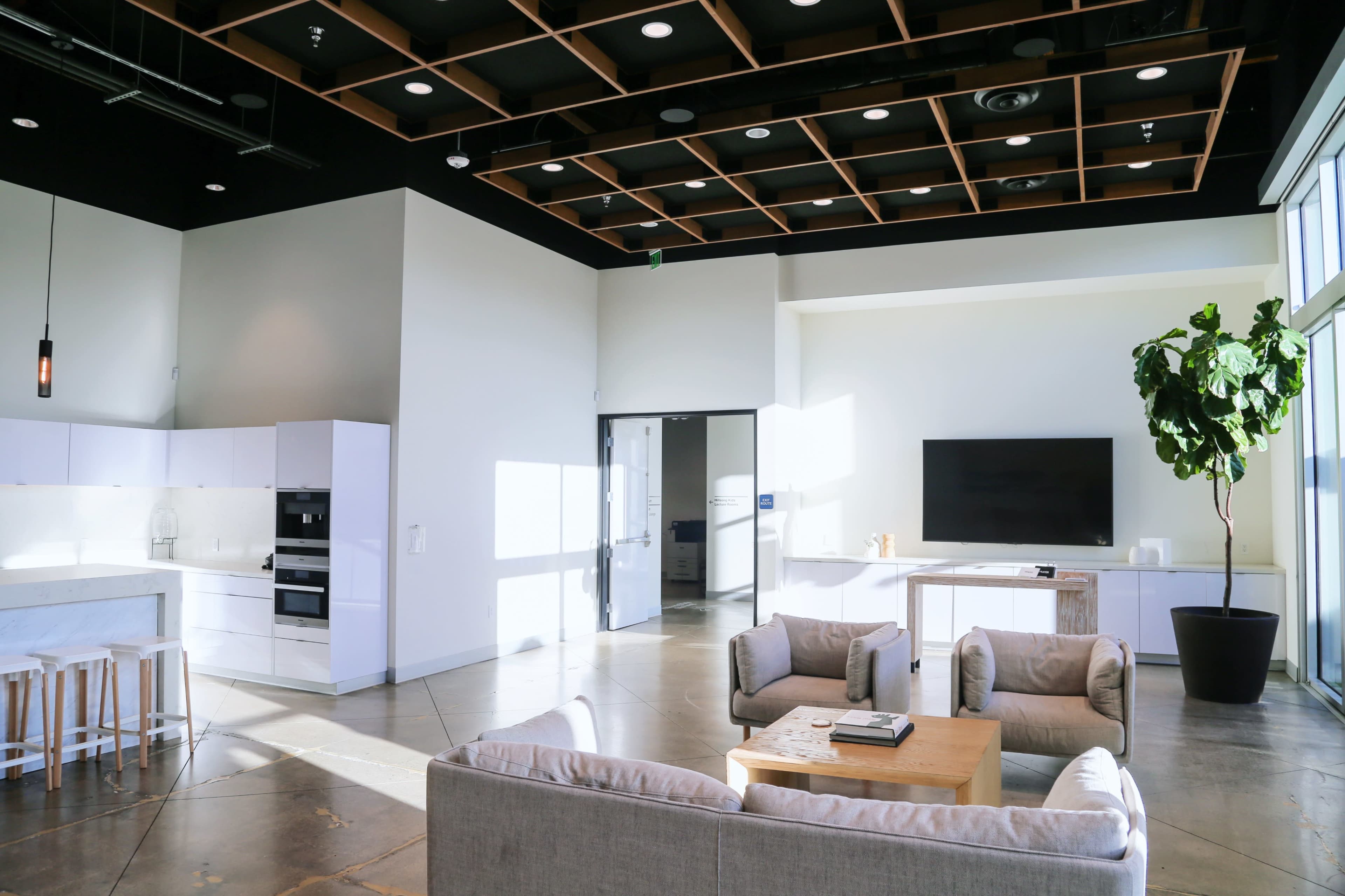 The image shows a modern open-concept living space with a kitchen, seating area, and large windows allowing natural light to enter.