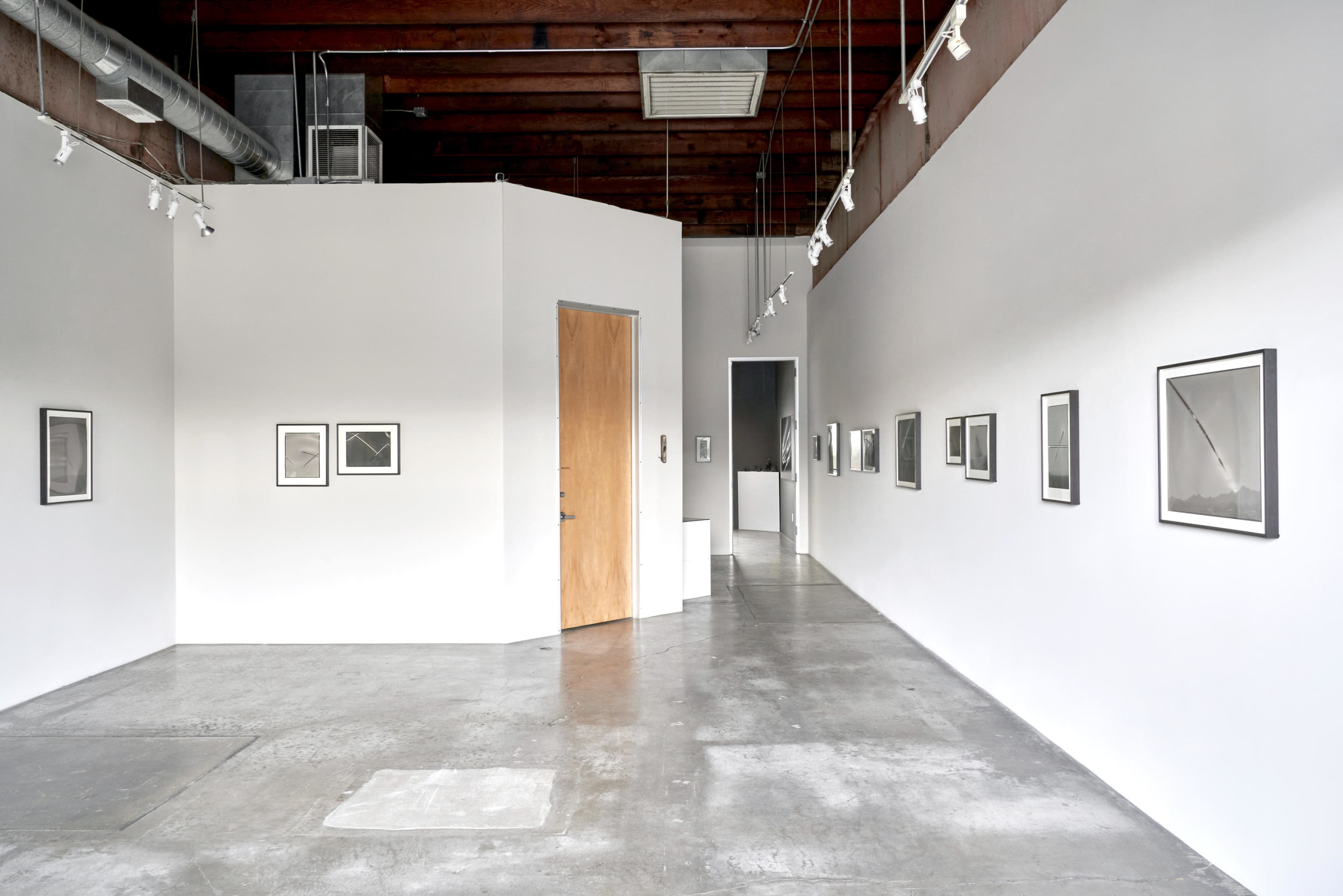 The image shows a modern art gallery featuring framed black and white photographs on white walls and a concrete floor.