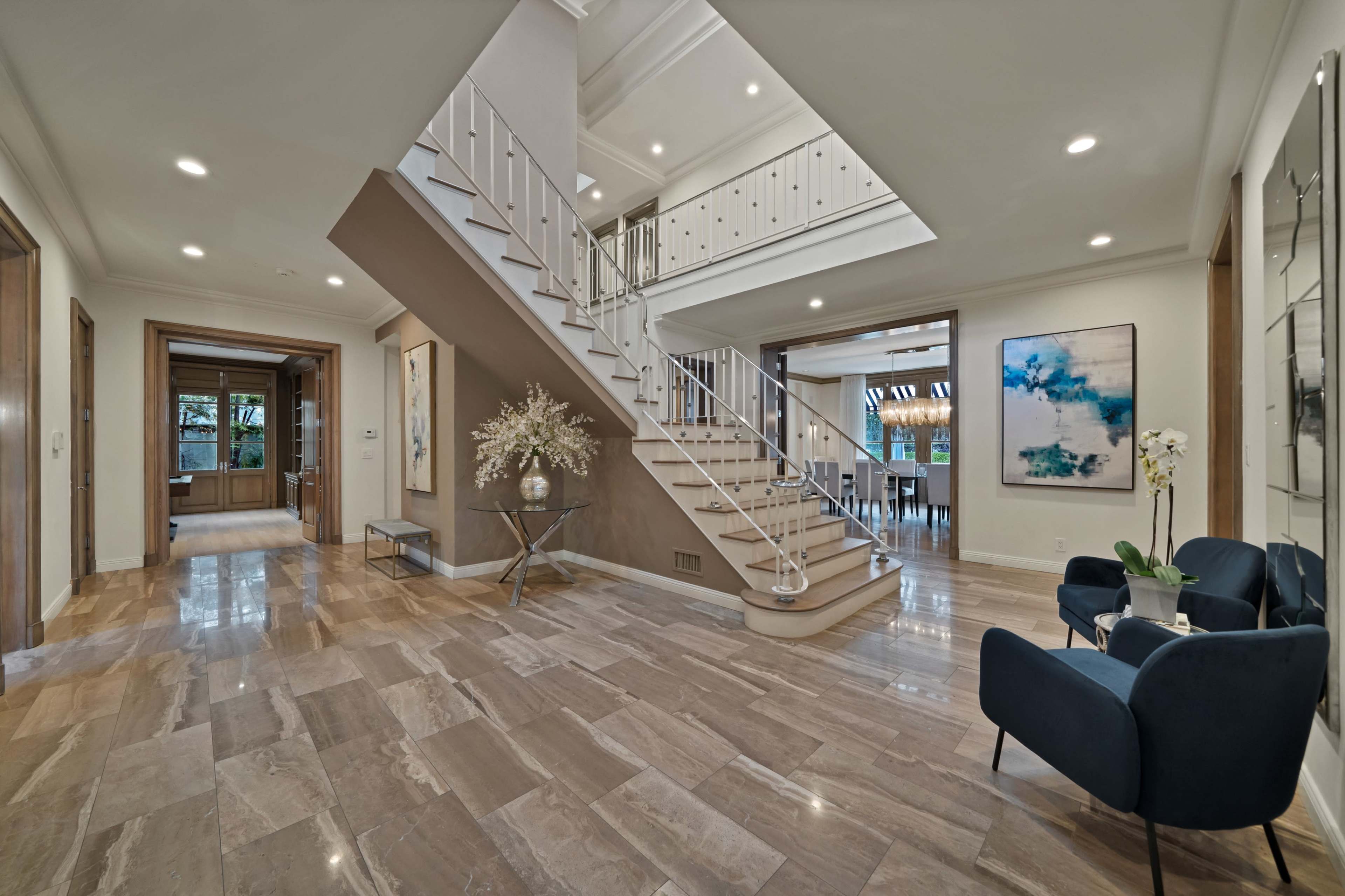 A spacious foyer features a two-story staircase, a polished stone floor, and modern artwork on the walls.