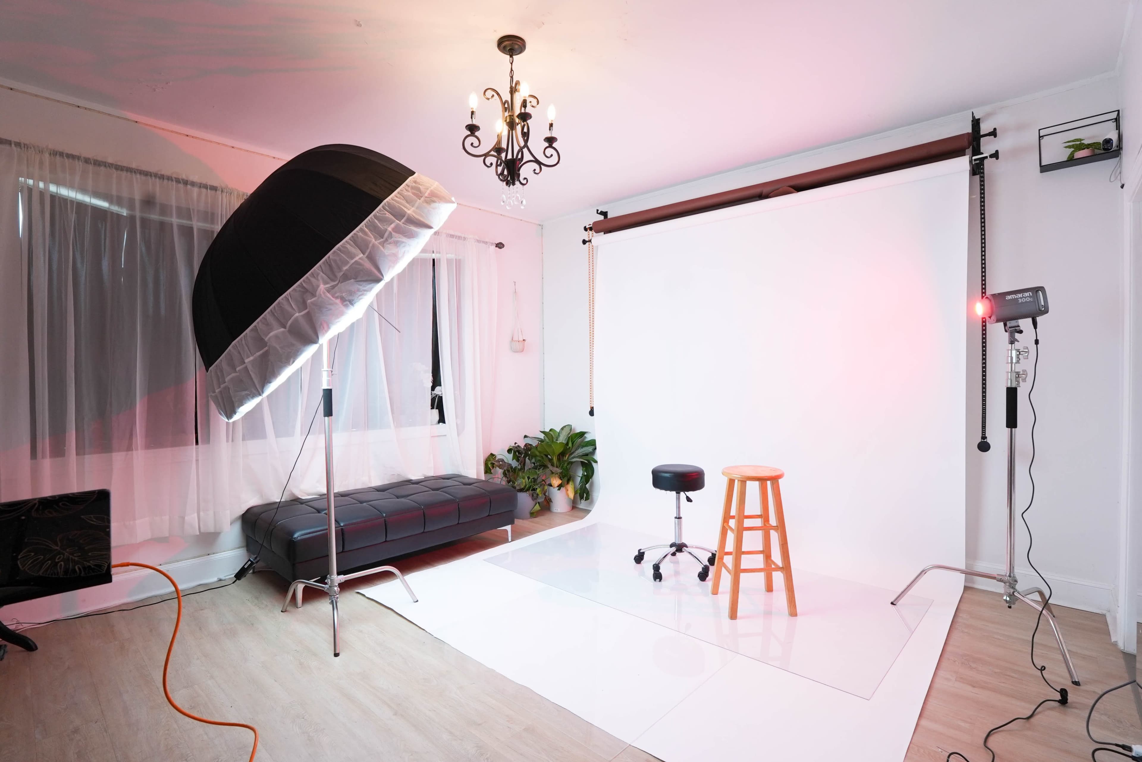 The image shows a photography studio with a large light reflector, a stool, and a white backdrop.