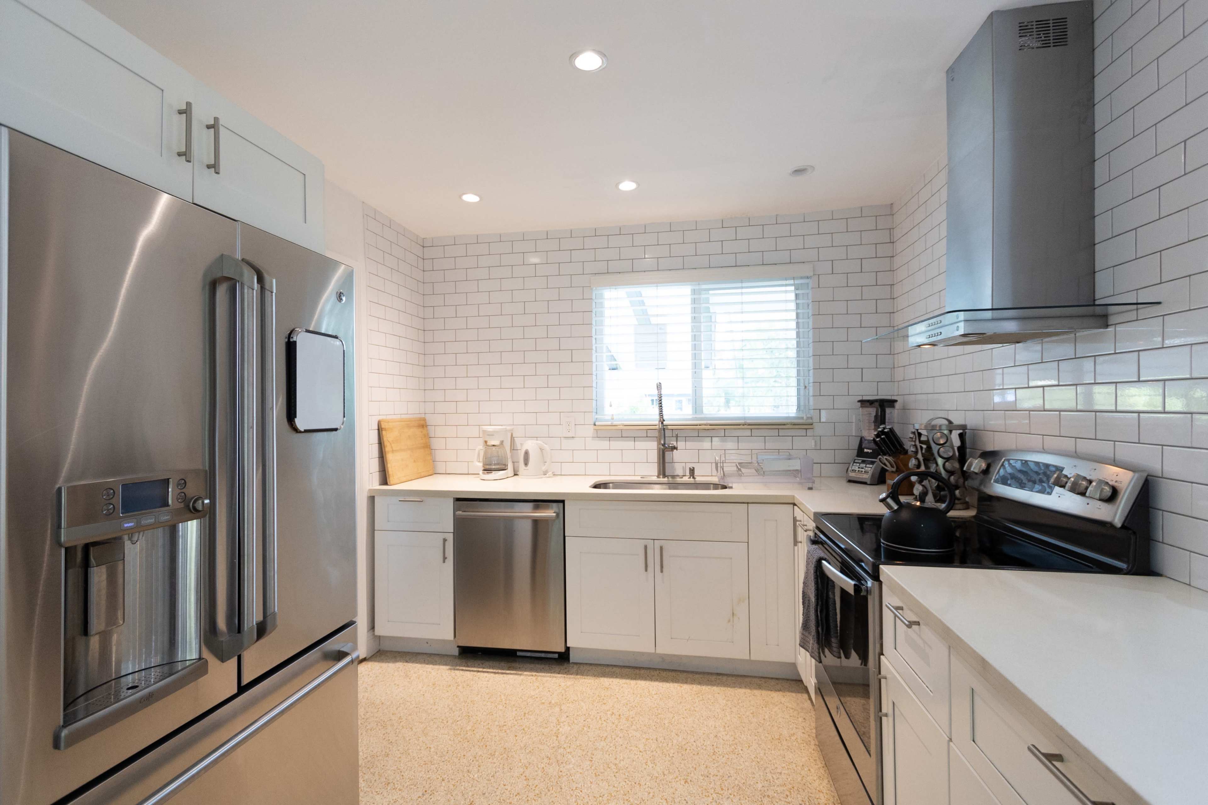 A modern kitchen featuring stainless steel appliances, white cabinetry, a tile backsplash, and a window above the sink.