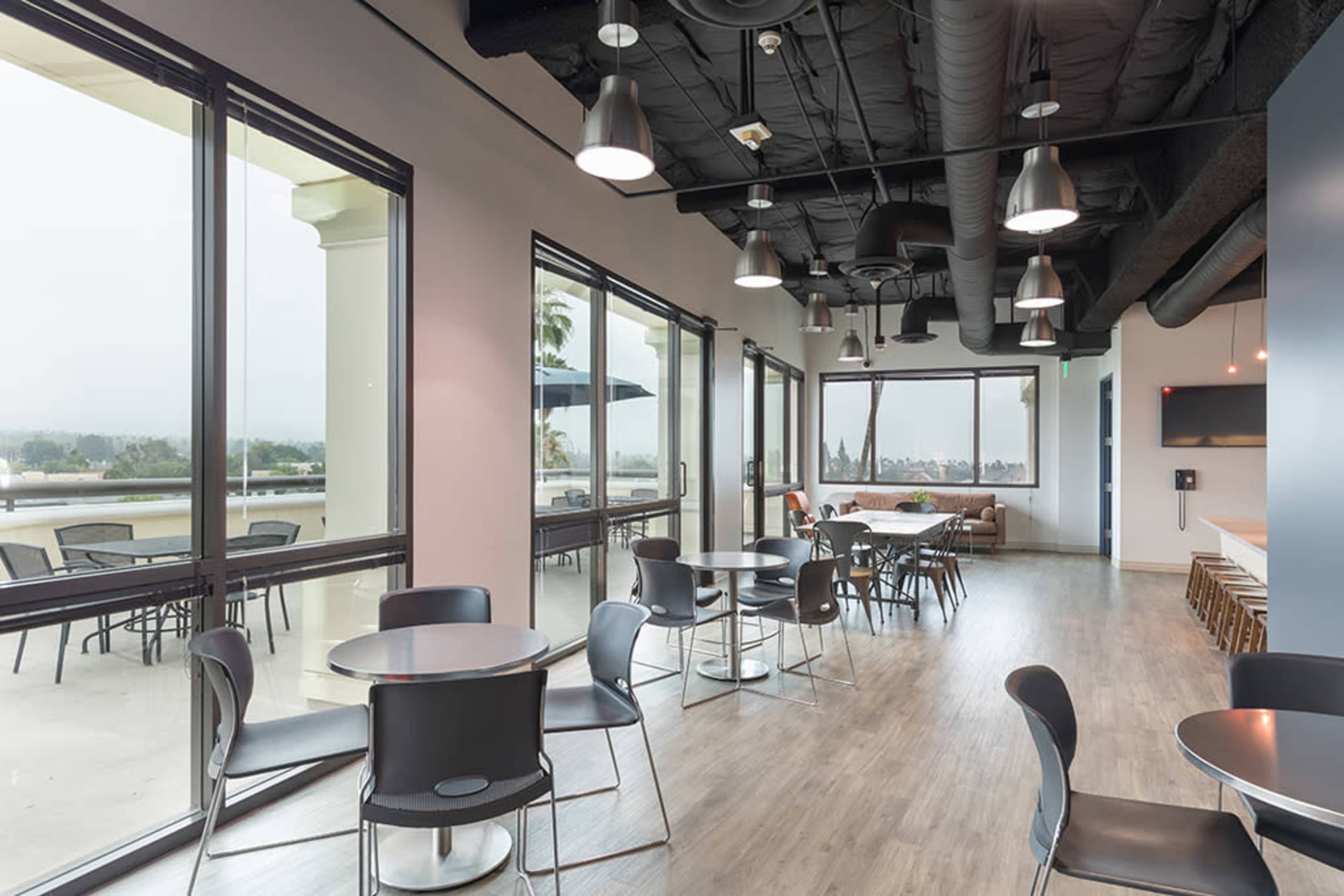 A modern indoor seating area with round tables and chairs, large windows providing natural light, and a minimalist design.