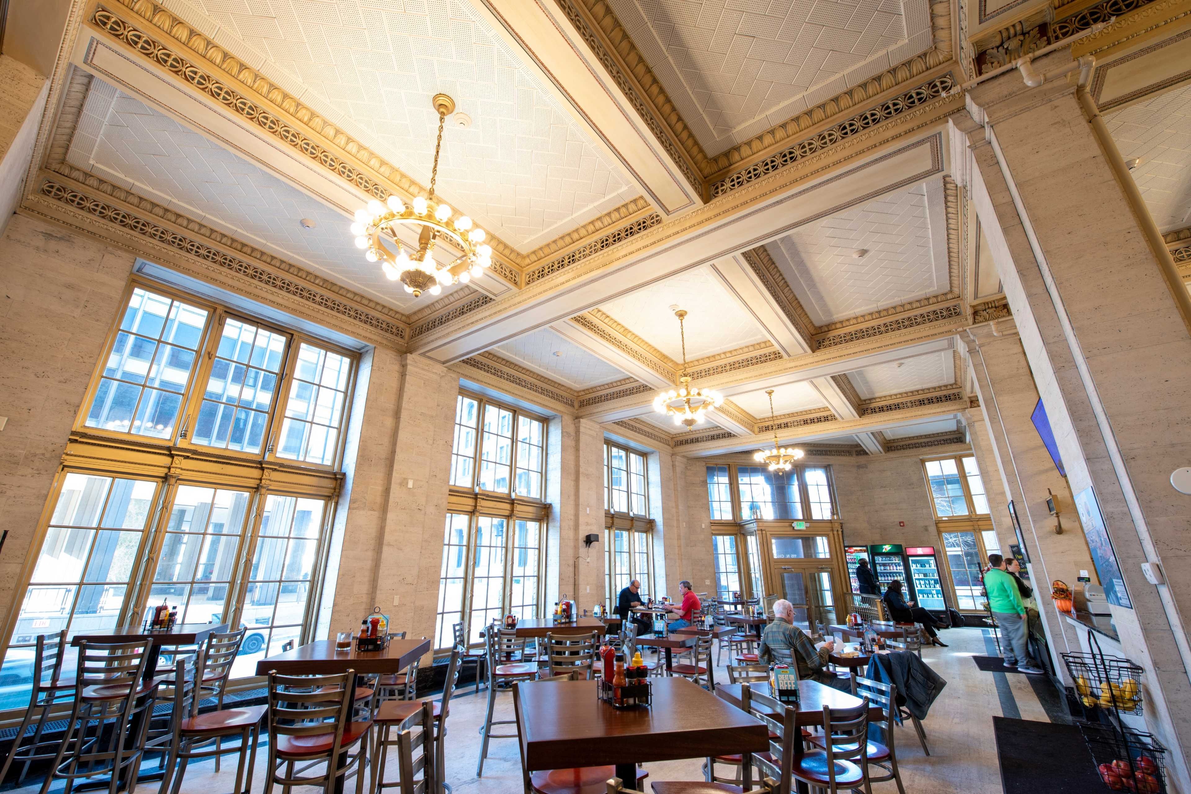 A spacious restaurant interior with large windows, high ceilings, and various seating arrangements.