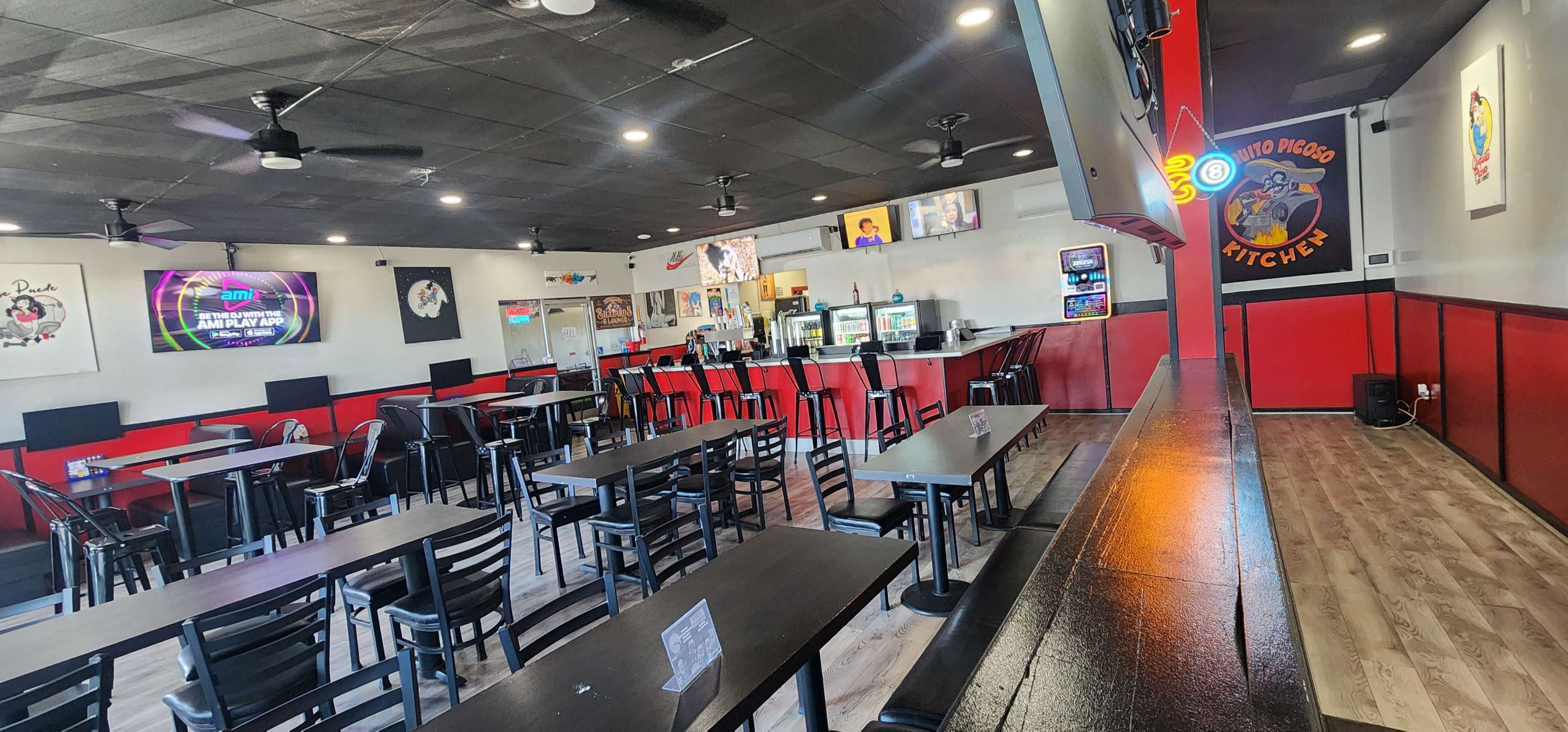 The image shows the interior of a restaurant featuring black tables and chairs, a red accent wall, and multiple screens displaying menus and promotions.