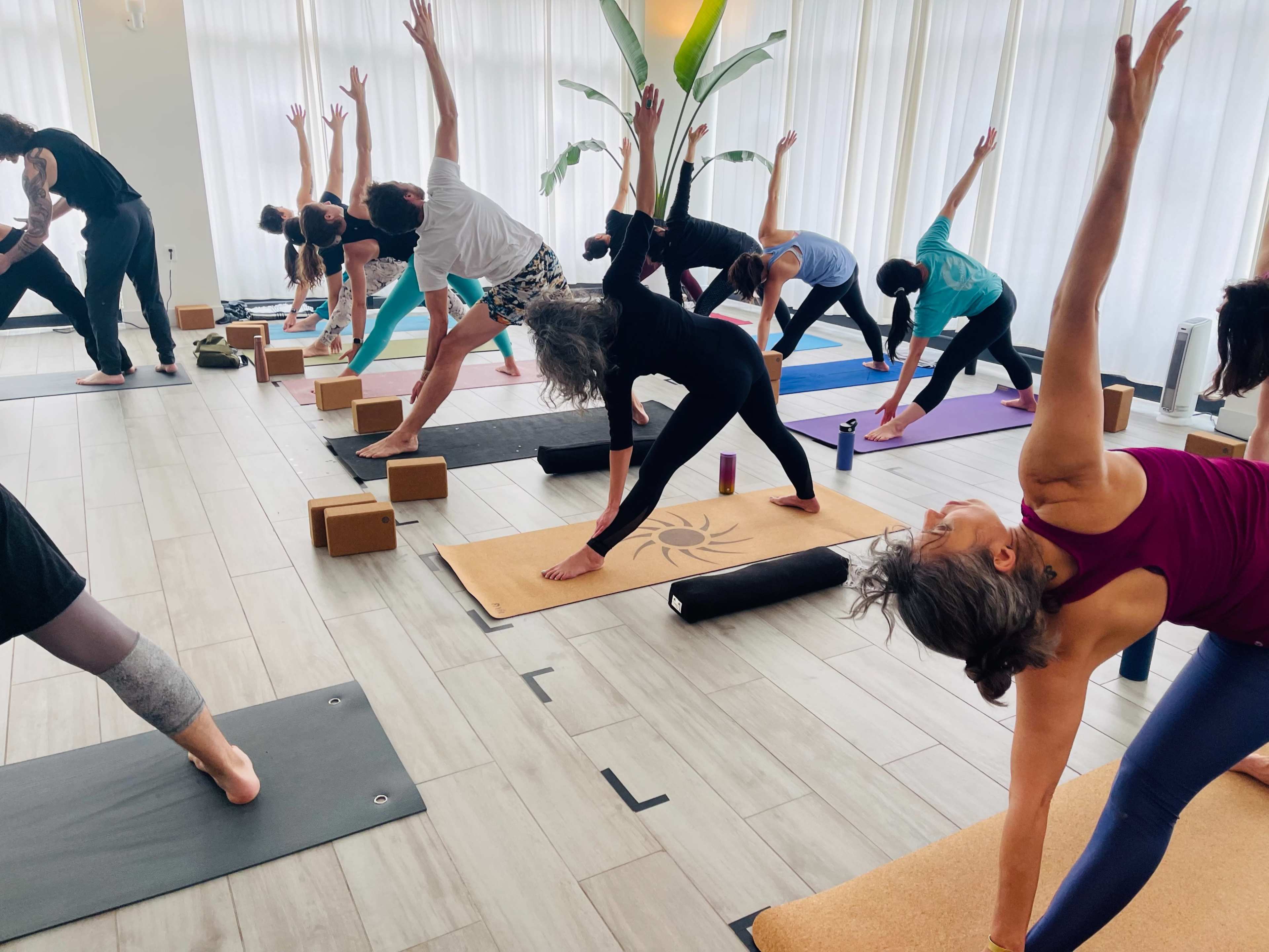 A group of people are practicing yoga in a warmly lit studio, using mats and blocks in various poses.