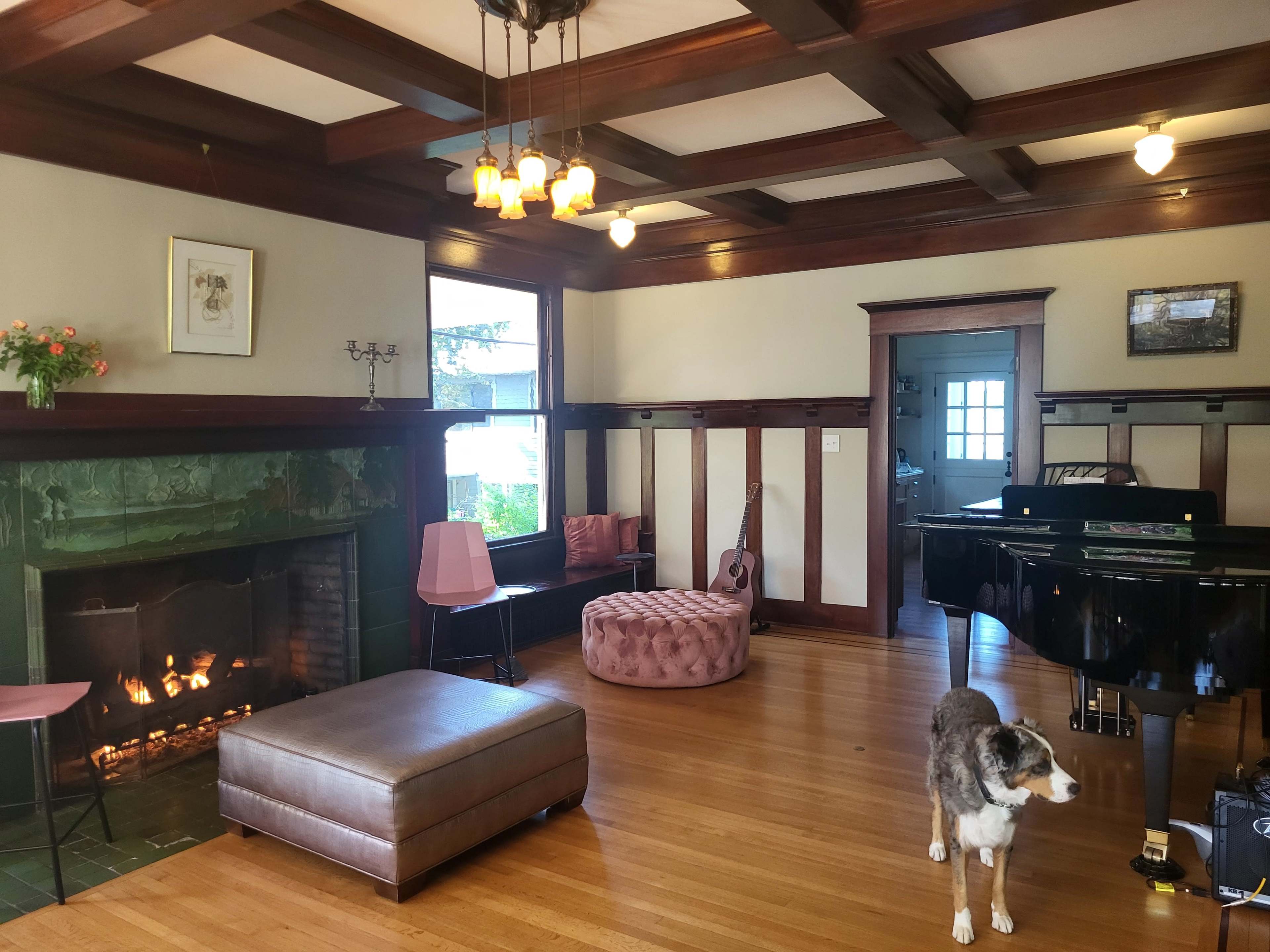 The living room features a fireplace, seating areas, a grand piano, and a dog standing on the hardwood floor.