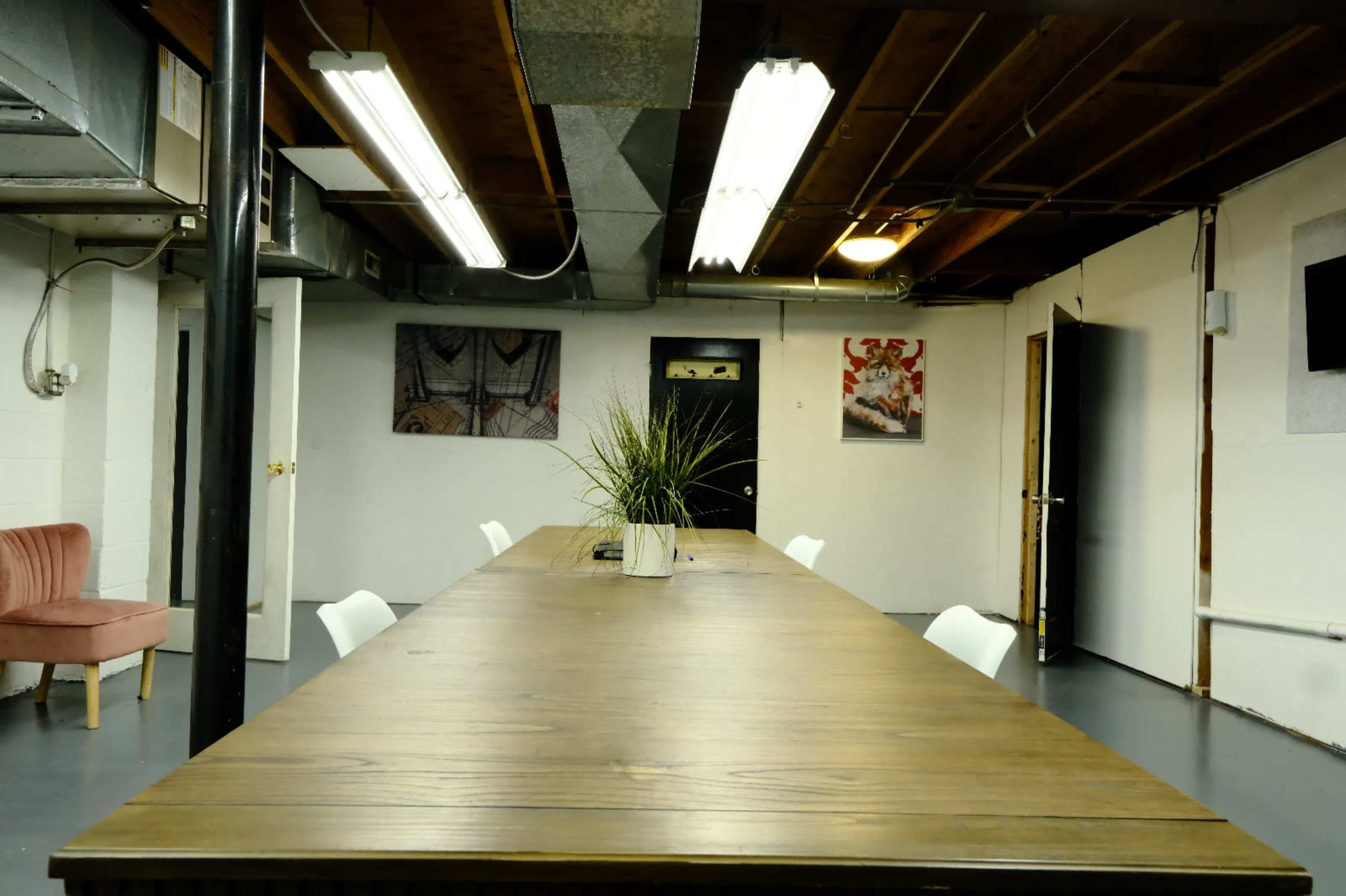 The image shows a spacious meeting room with a long wooden table, white chairs, and various artworks displayed on the walls.