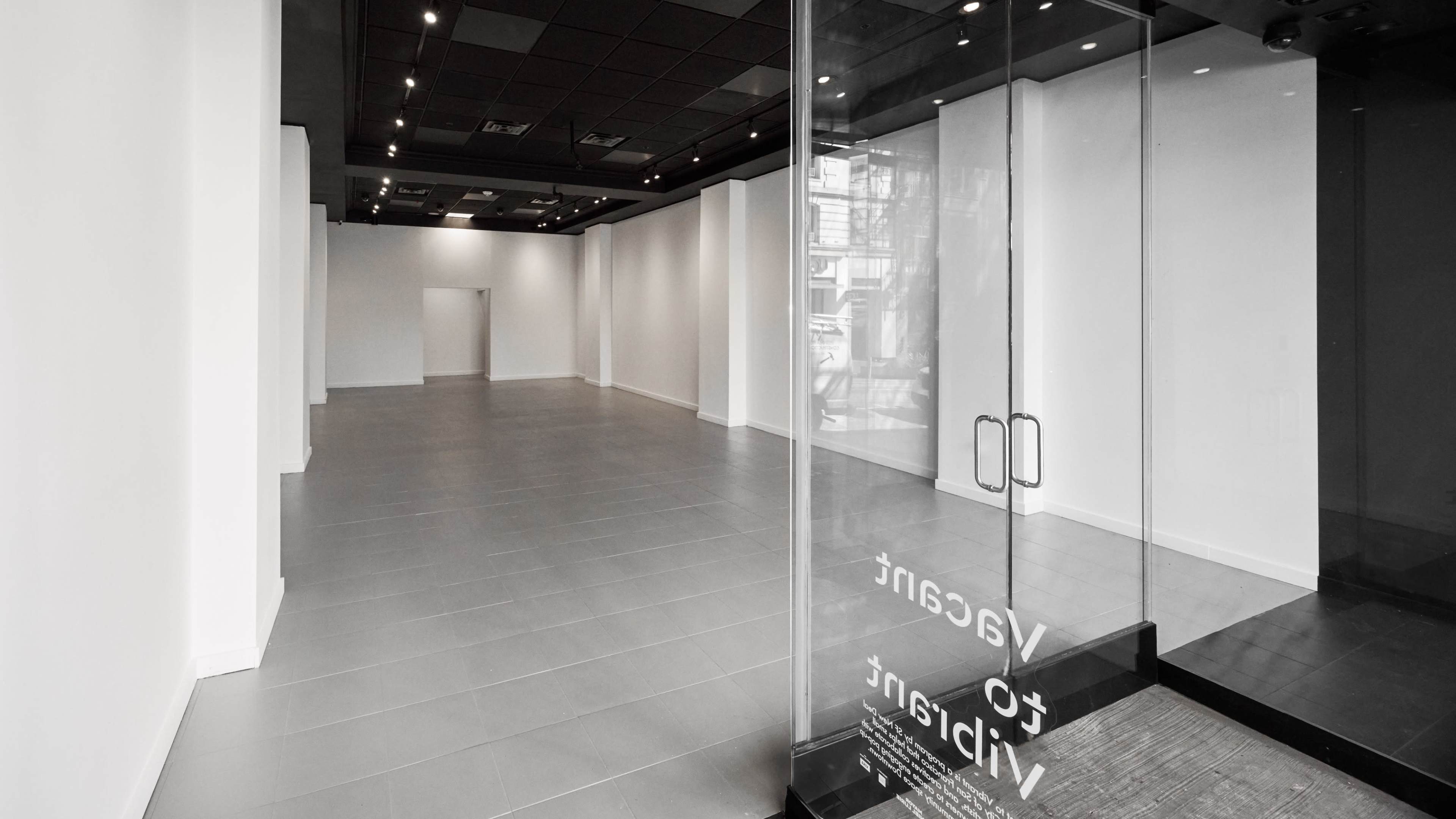 The image shows an empty, well-lit retail space with tile flooring and large glass entrance doors.
