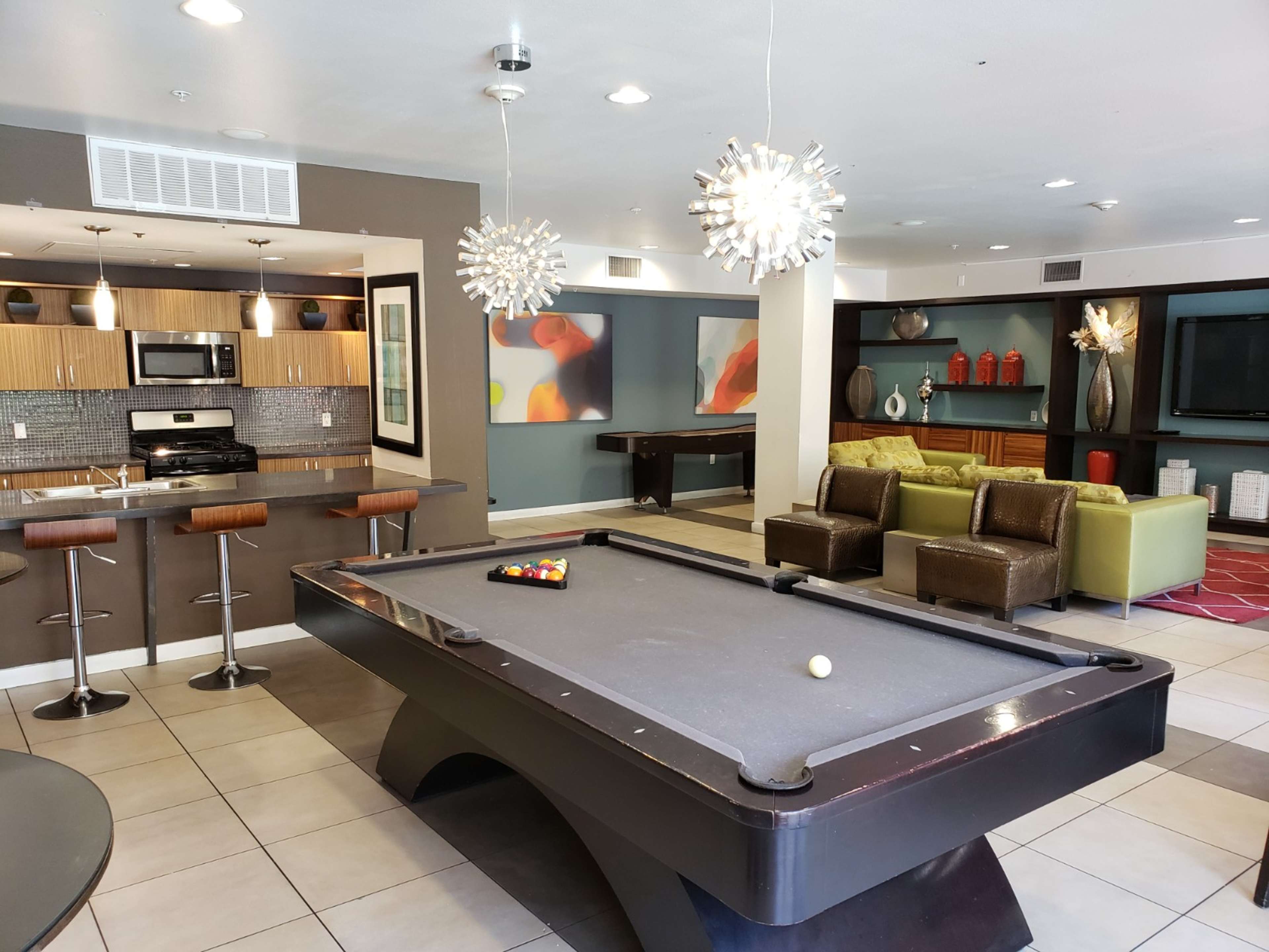 A modern recreation room featuring a billiards table, a kitchen area with bar stools, and colorful furniture.