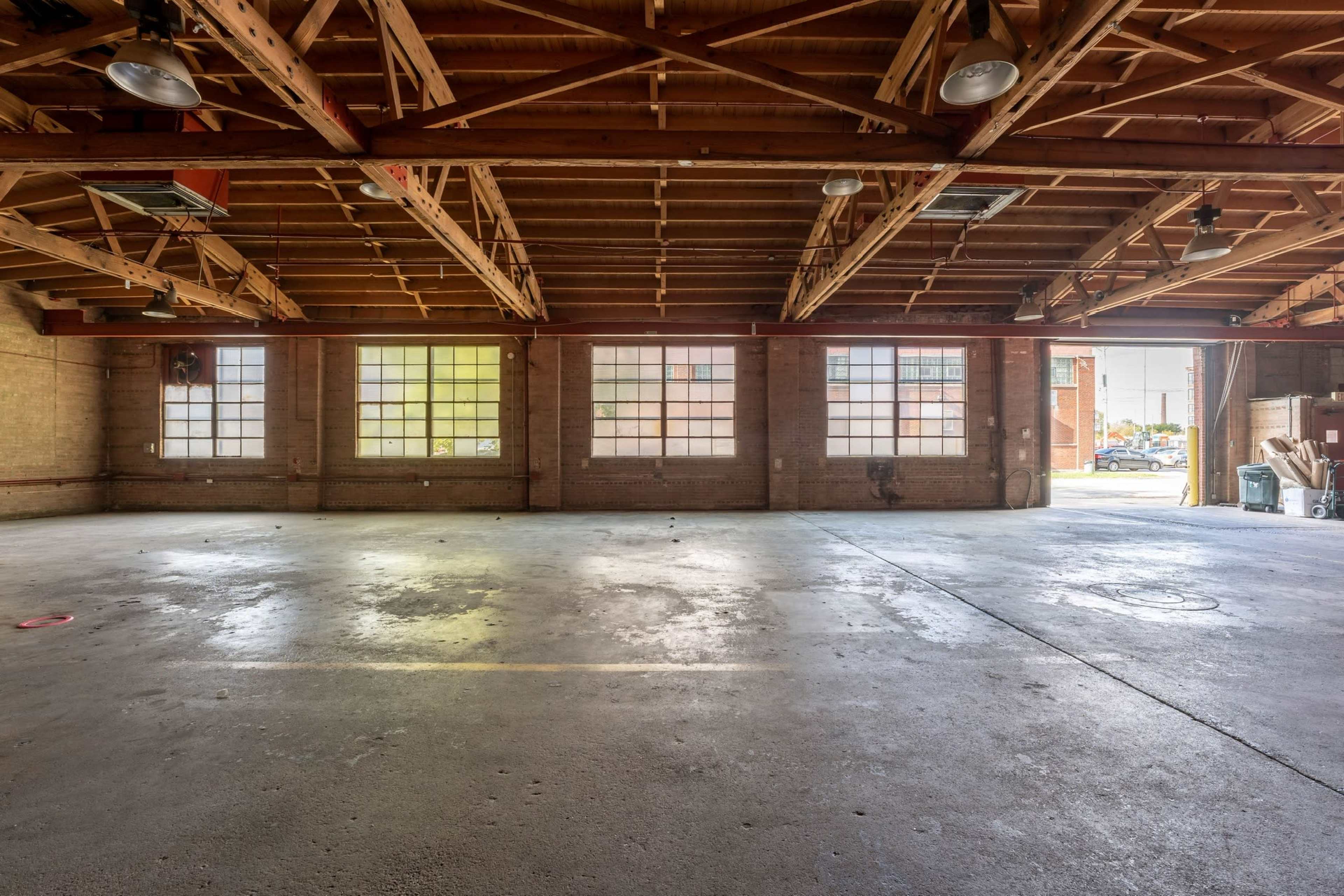 The image shows a spacious, empty garage with large windows allowing natural light to enter.
