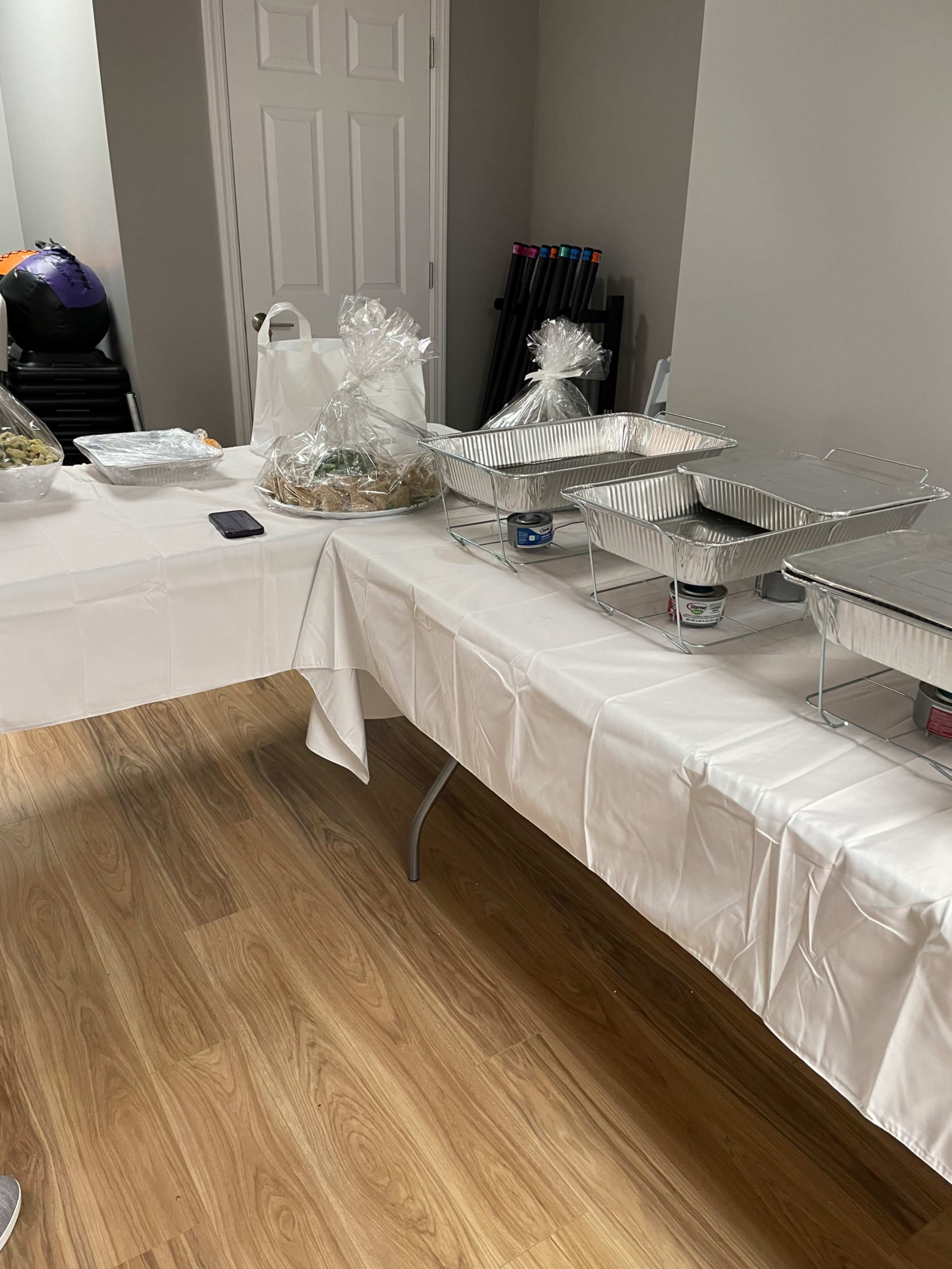 A table is set with various food dishes and containers covered with aluminum foil in a well-lit room.