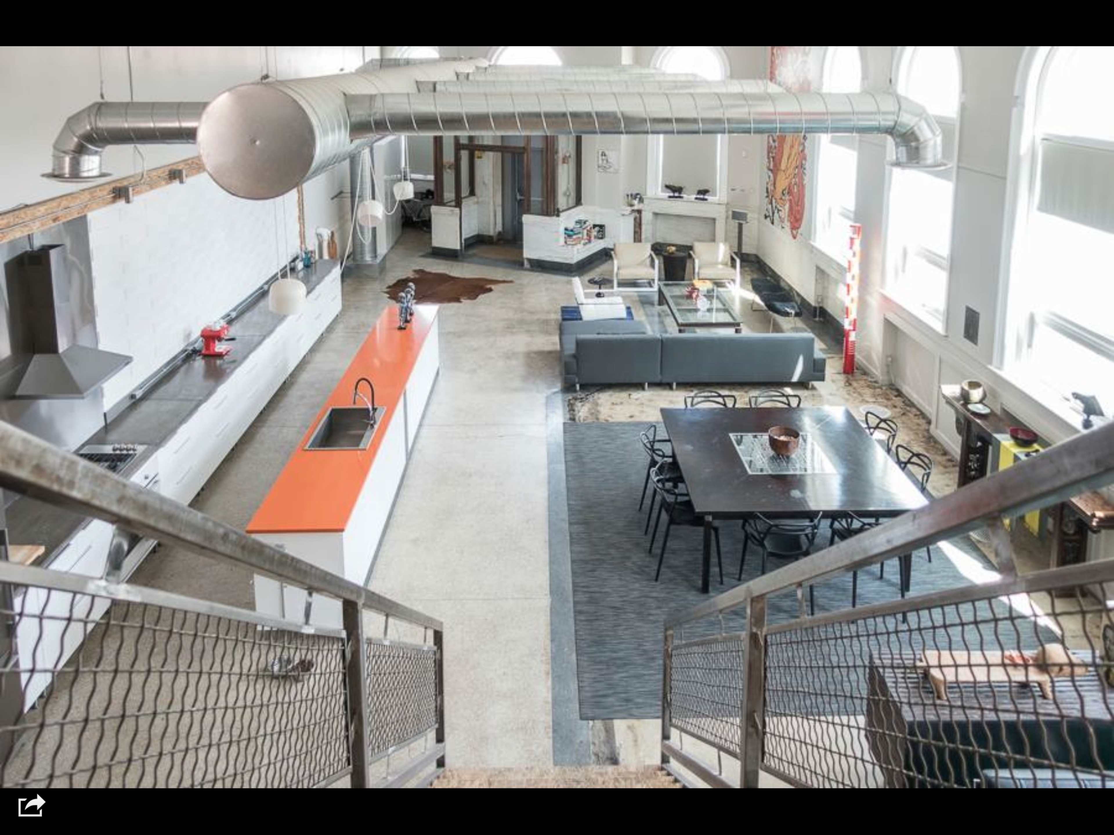A spacious, modern kitchen and living area with an orange countertop, a large dining table, and a gray sectional sofa.