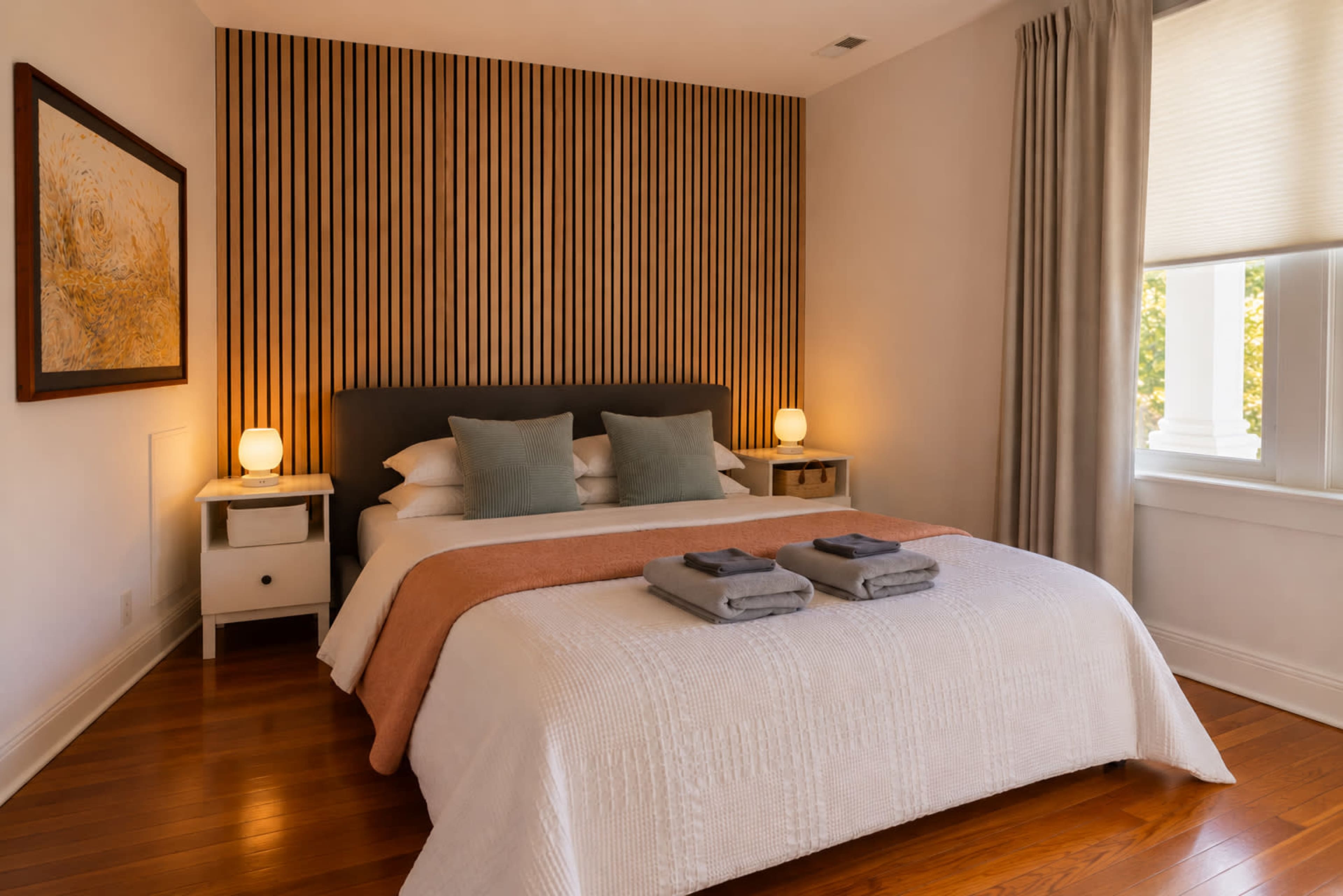 The image shows a neatly arranged bedroom featuring a bed with decorative pillows, a textured wall behind the bed, and soft bedside lighting.