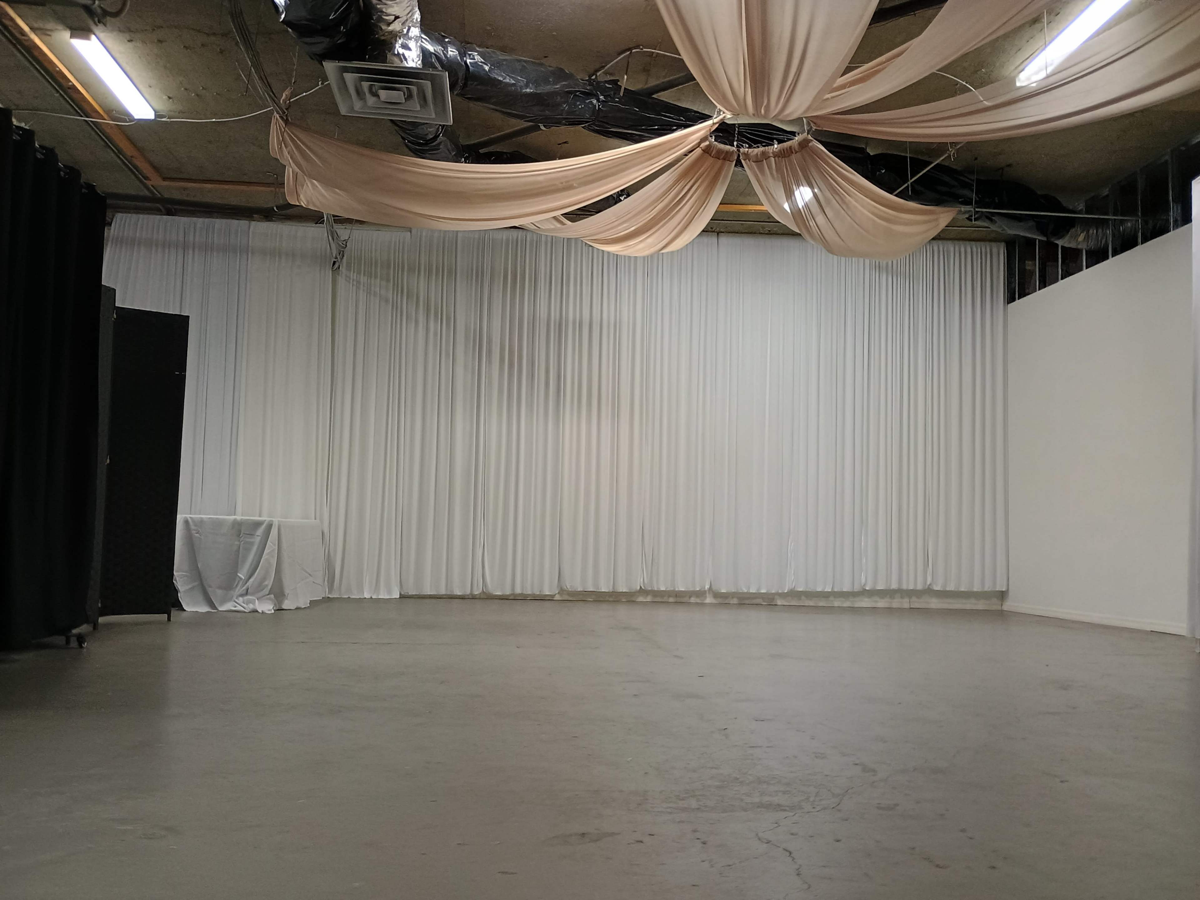The image shows a spacious room with a polished concrete floor and white drapery hanging from the ceiling.