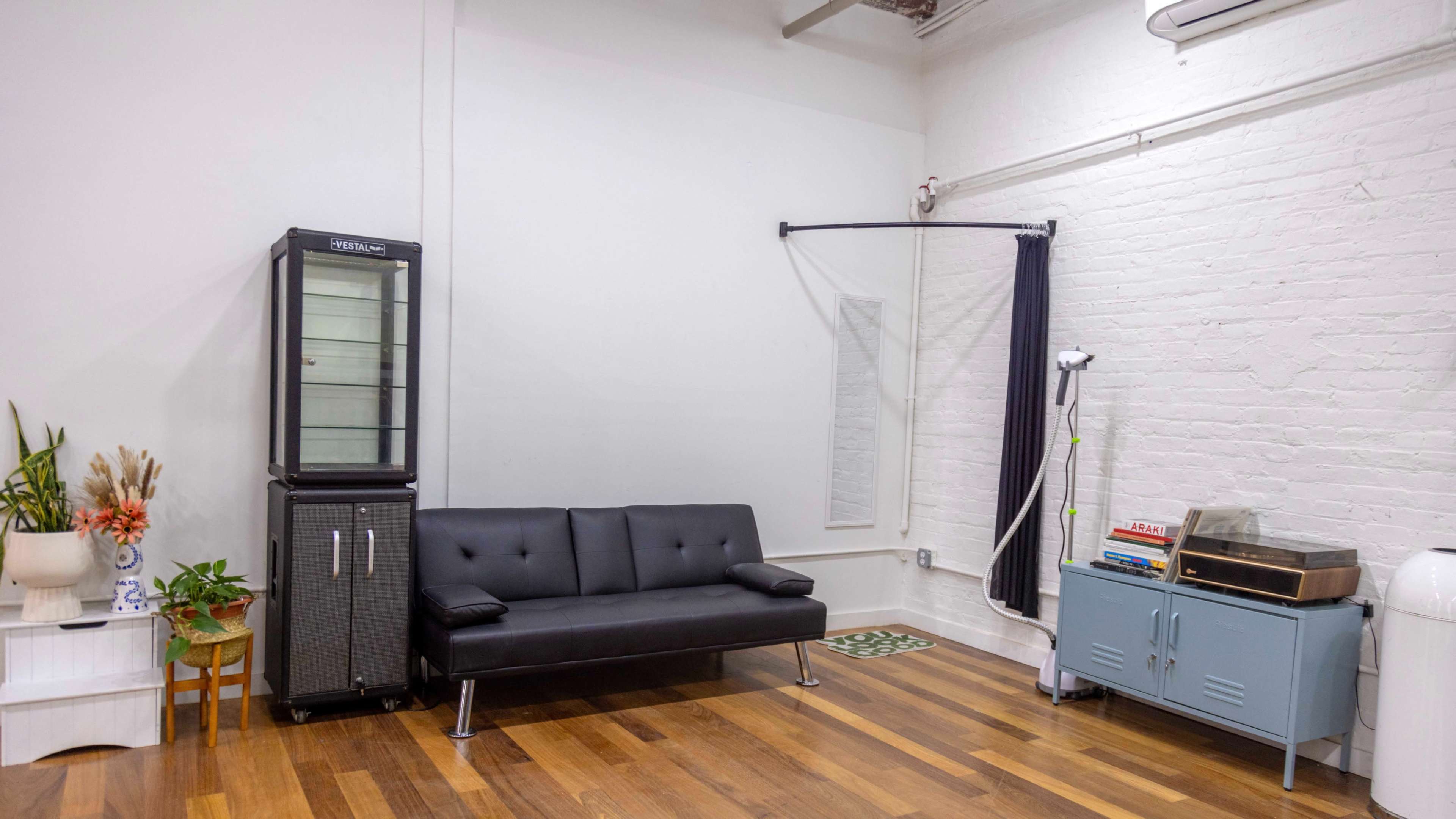 A minimalist room with a black sofa, a glass-front cabinet, a vintage record player, and a potted plant on a wooden floor.