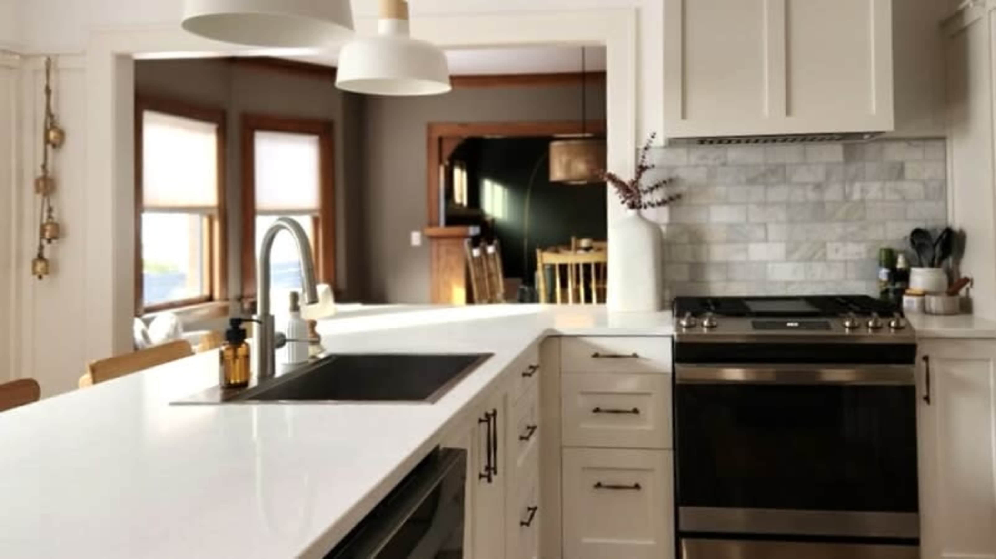 The image shows a modern kitchen with white cabinets, a large countertop, and stainless steel appliances.