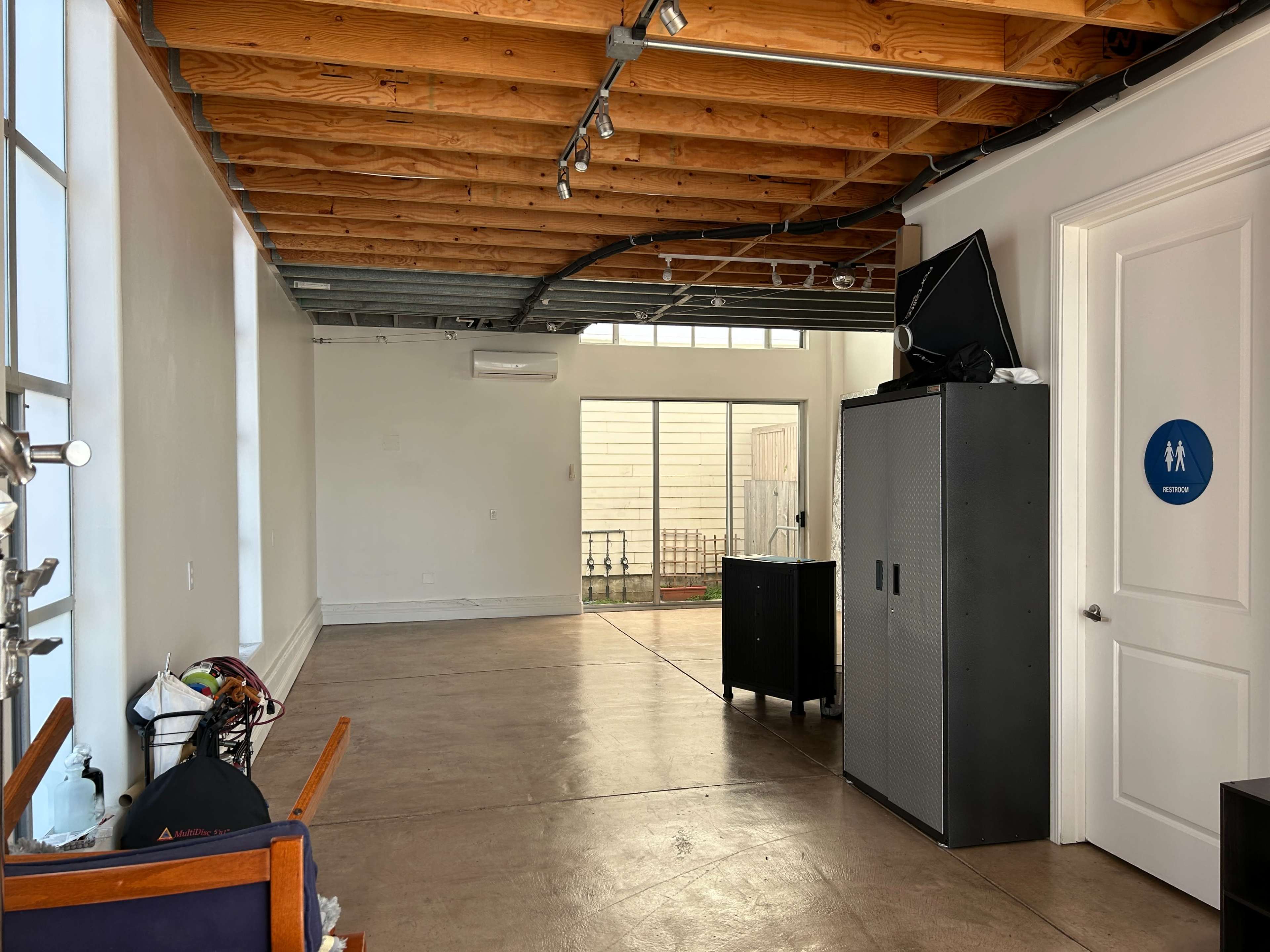 A spacious, empty interior with exposed wooden beams, a couple of furniture items, and a door leading to an outdoor area.
