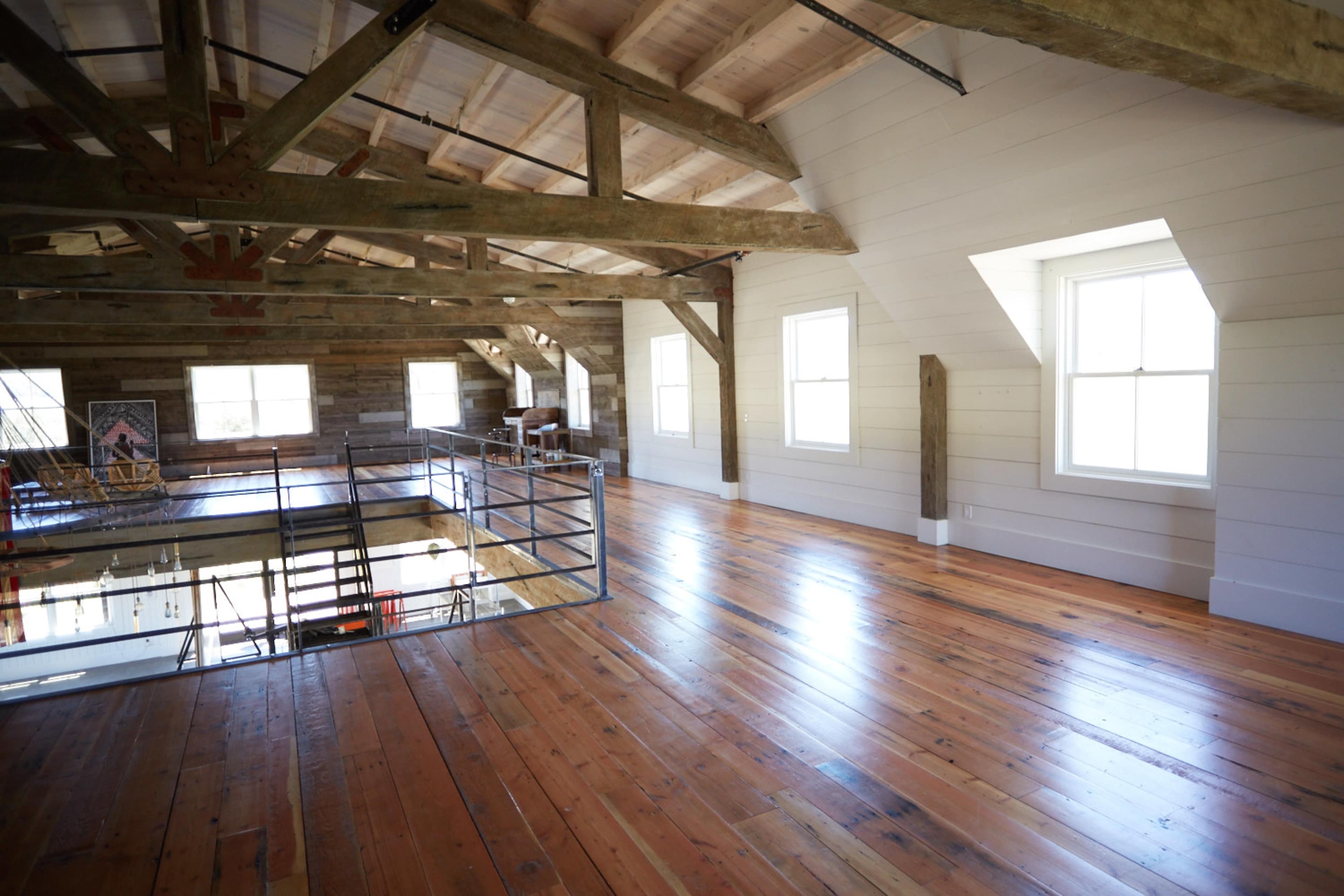 An empty, spacious interior of a loft with wooden beams and polished wooden floors, illuminated by natural light from large windows.