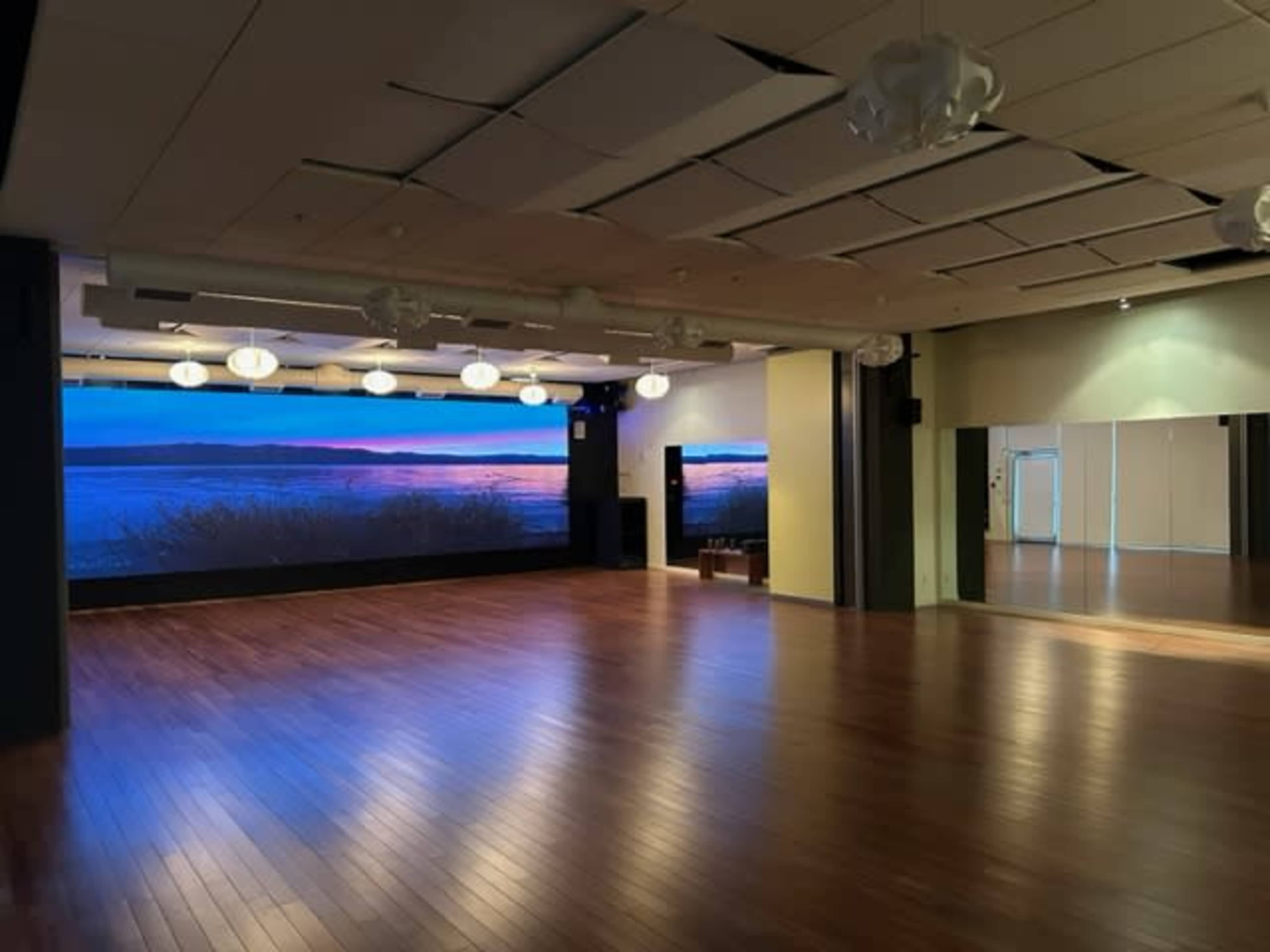 An empty room with polished wooden floors, large screens displaying a landscape, and a wall of mirrors.