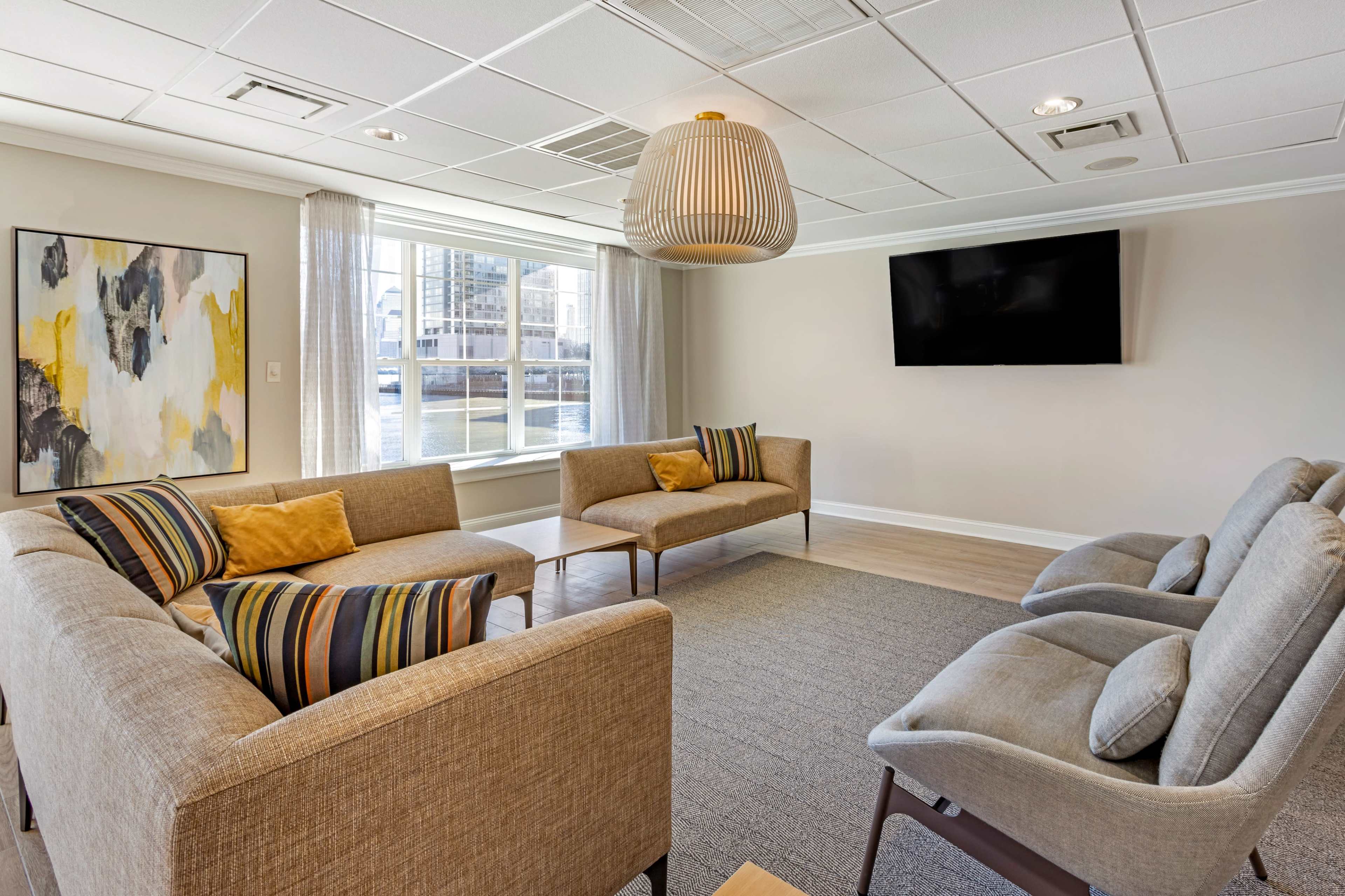 A modern lounge area with two beige sofas, a coffee table, and a large window overlooking a waterfront view.