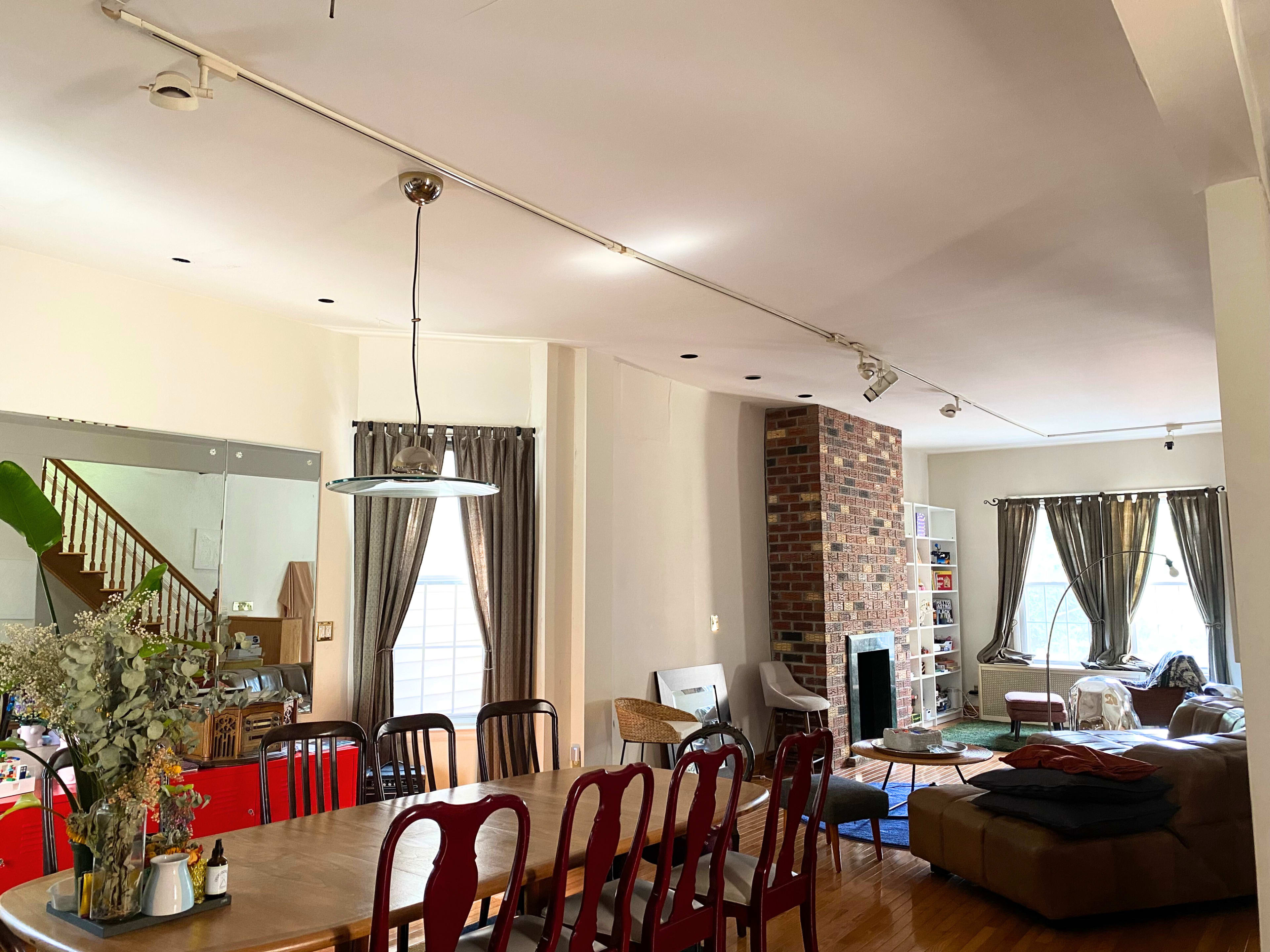 A spacious living area with a dining table, a comfortable seating area, a brick fireplace, and large windows with curtains.