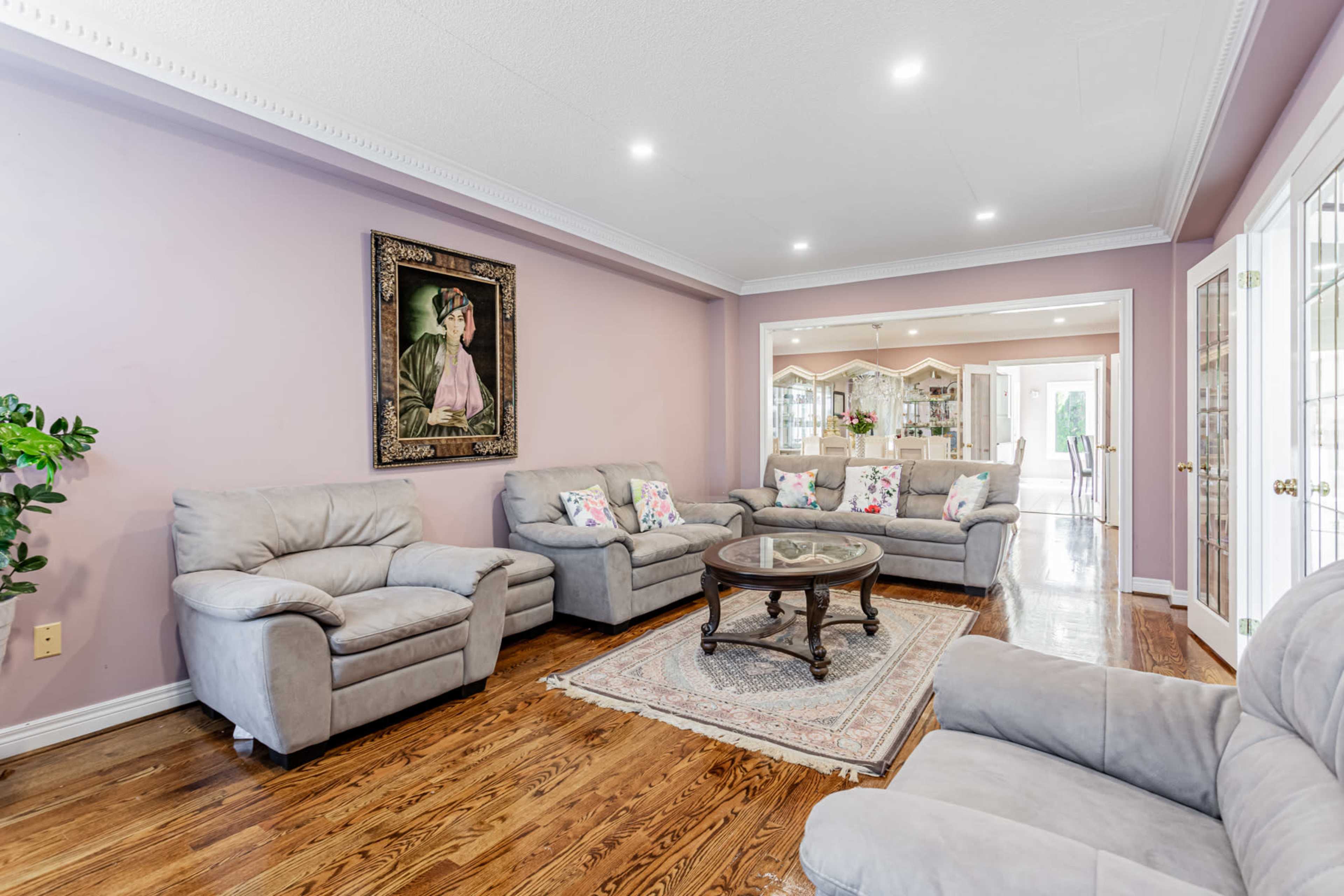 The living room features light gray sofas arranged around a round wooden coffee table on a decorative rug, with a framed portrait hanging on the wall.