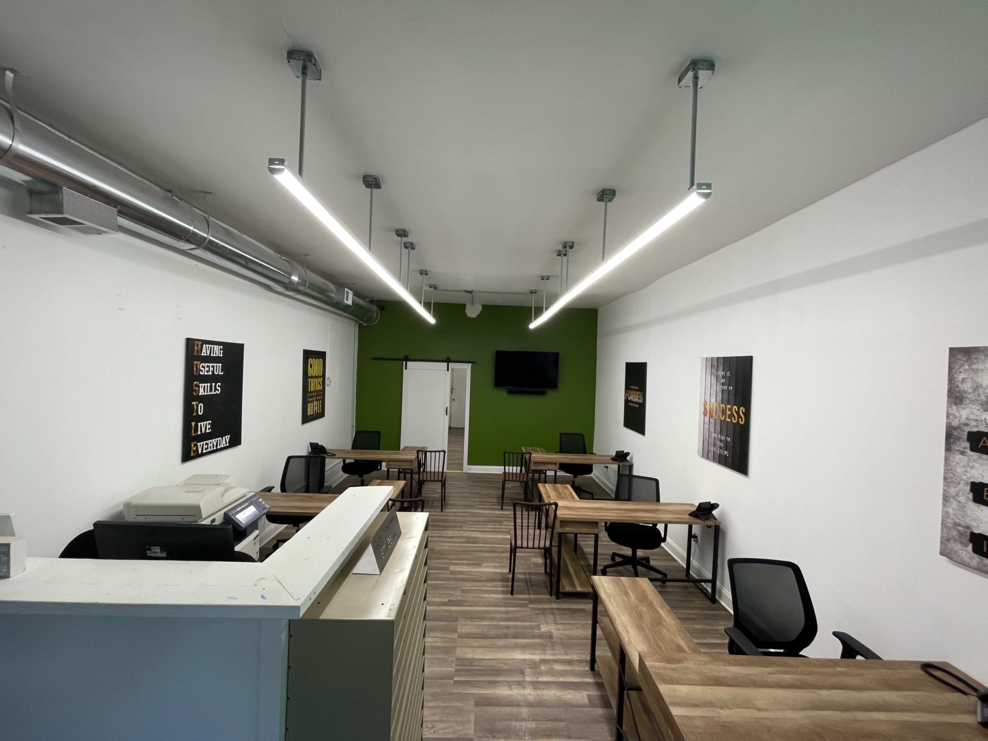 A modern office space with multiple workstations, a reception area, and a large green accent wall.