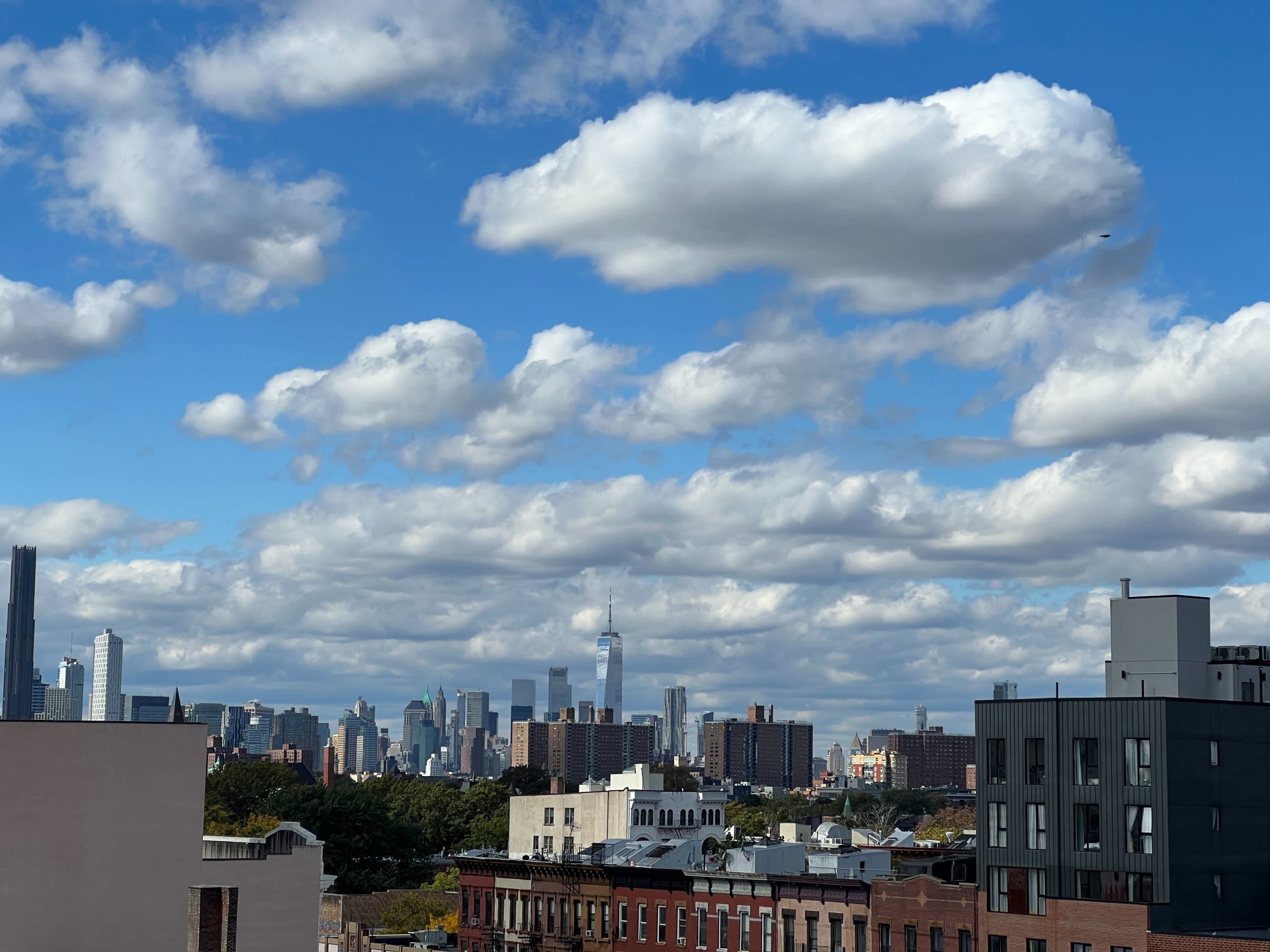 The image shows a city skyline with tall buildings under a sky filled with fluffy clouds.