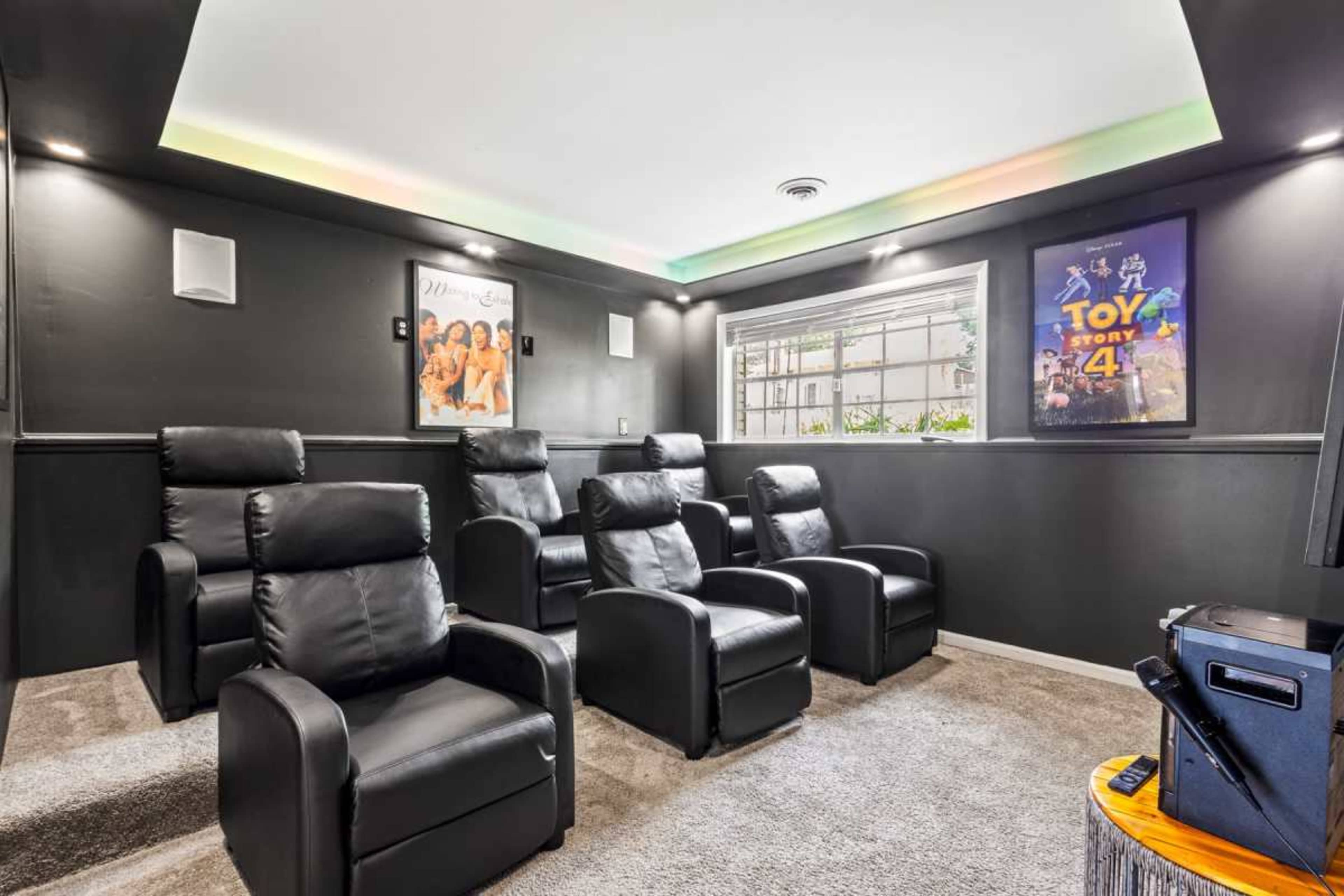 The image shows a home theater room with black leather seating, a window, and movie posters on the walls.
