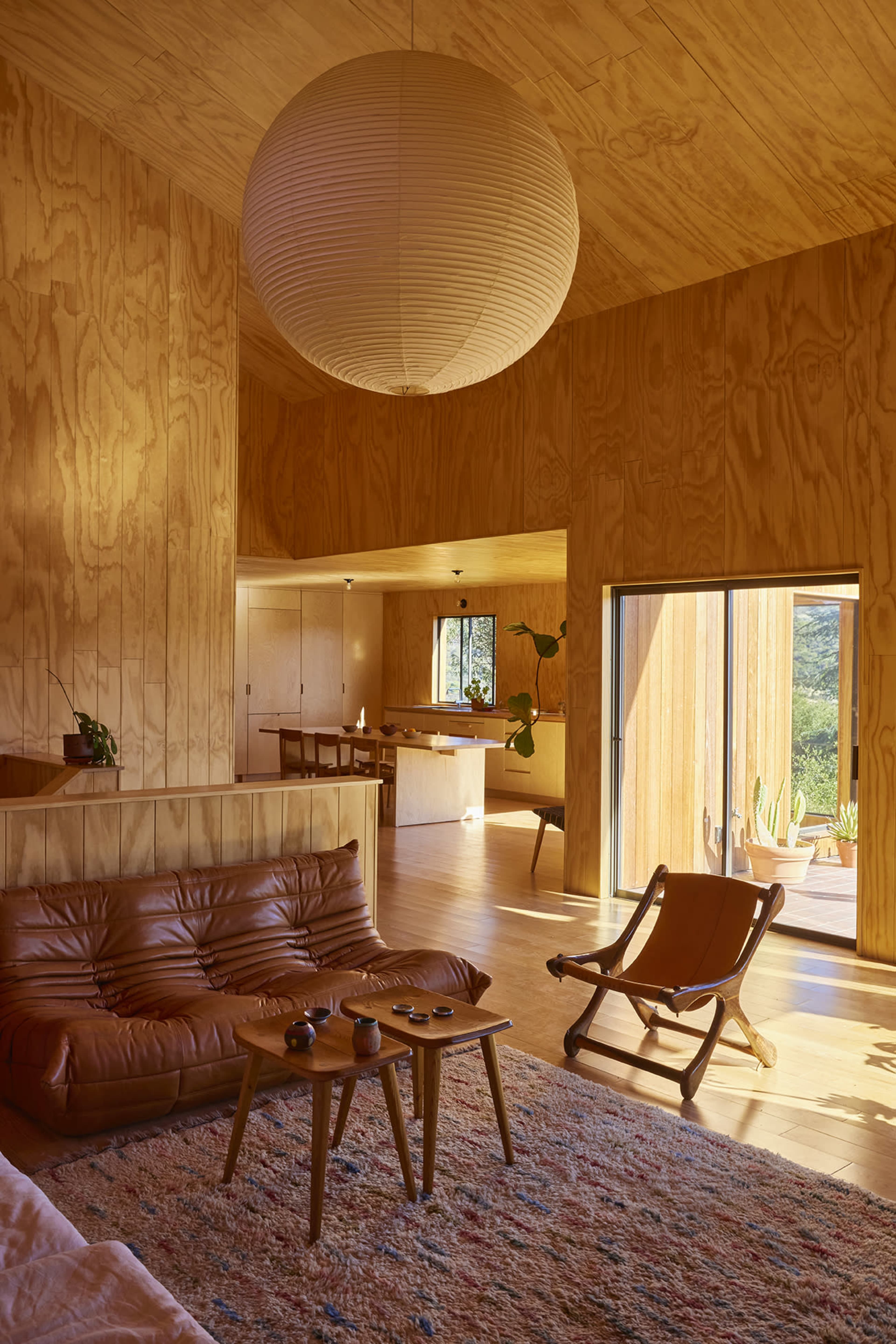 A modern interior space featuring wooden walls, a leather sofa, a rocking chair, and a large paper lantern hanging from the ceiling.