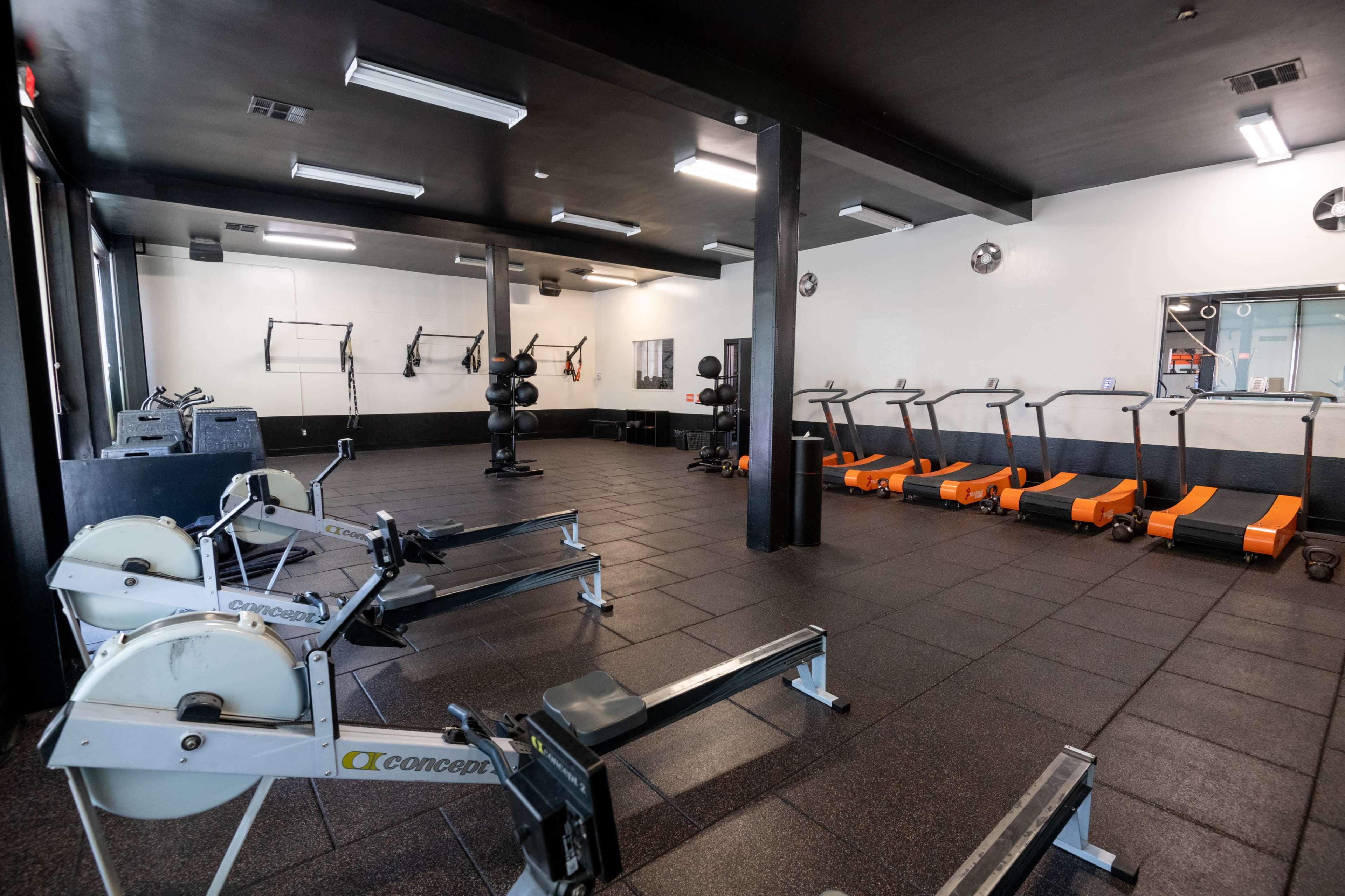 The image shows a fitness gym featuring rowing machines, treadmills, and free weights arranged on a rubber floor.