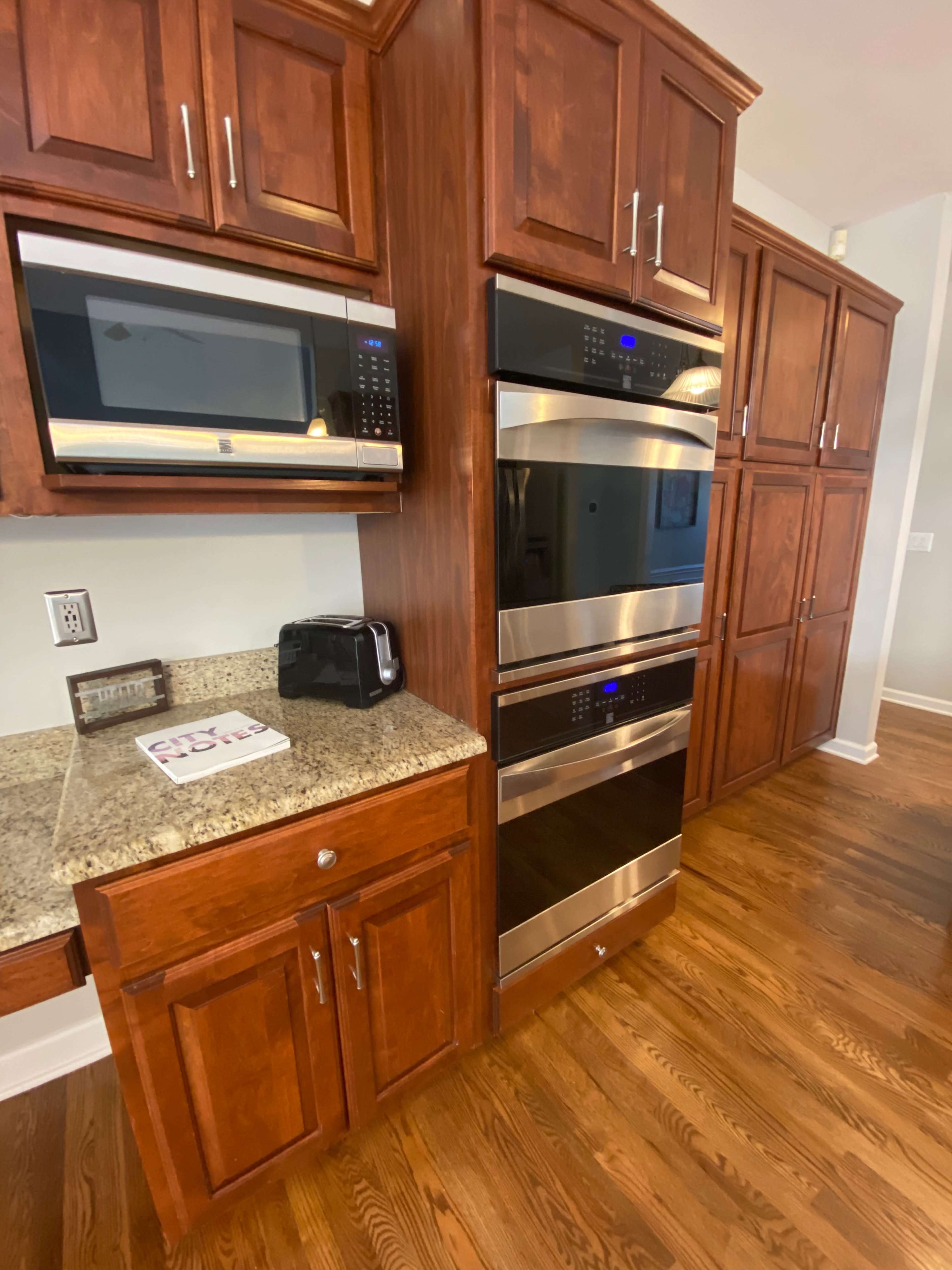 A modern kitchen with wooden cabinetry, a microwave, and a double wall oven integrated into the cabinetry next to a countertop.