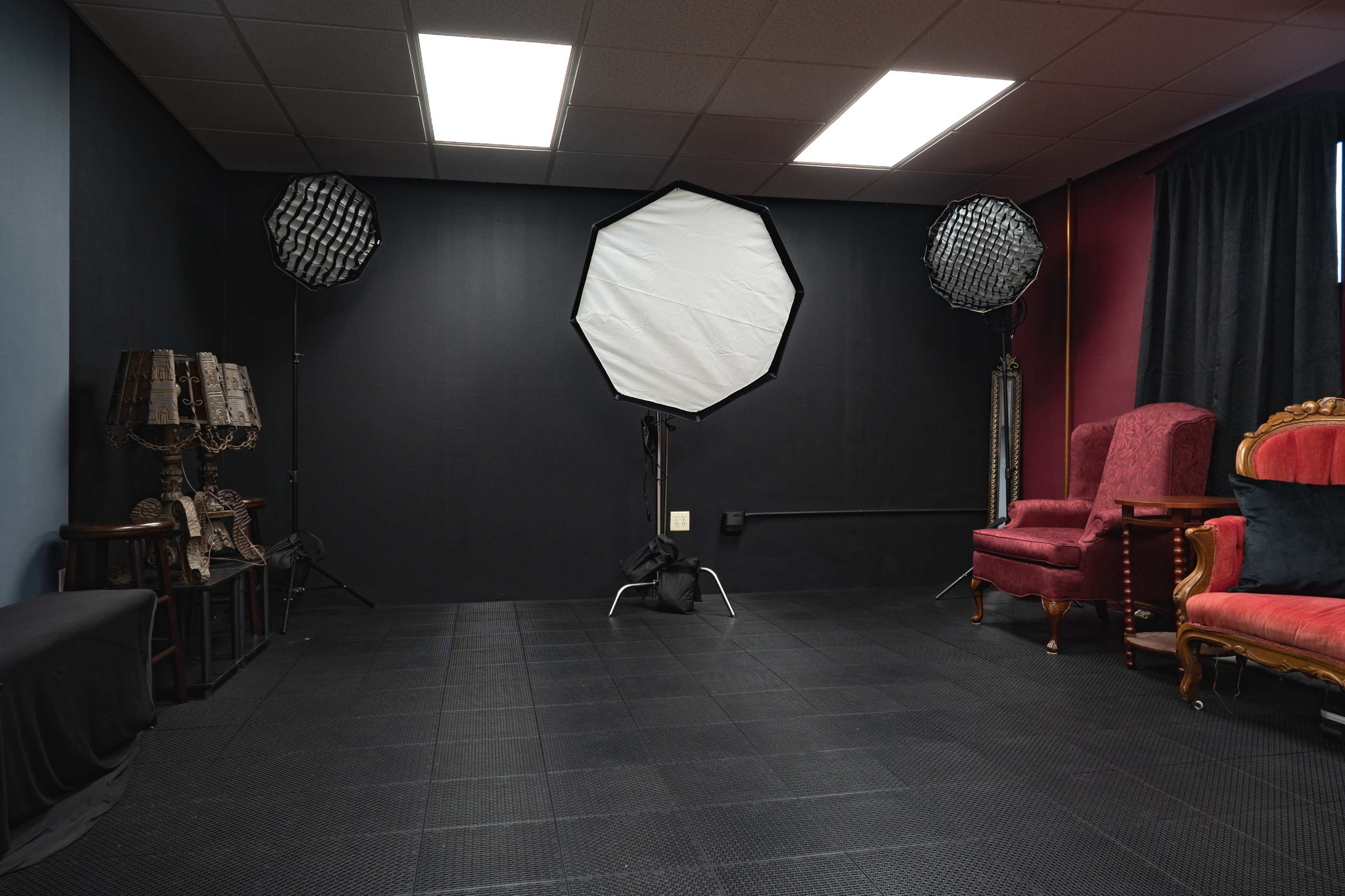 The image shows a photography studio with two softbox lights and a red and gold Victorian-style chair opposite a decorative lamp and a bench.