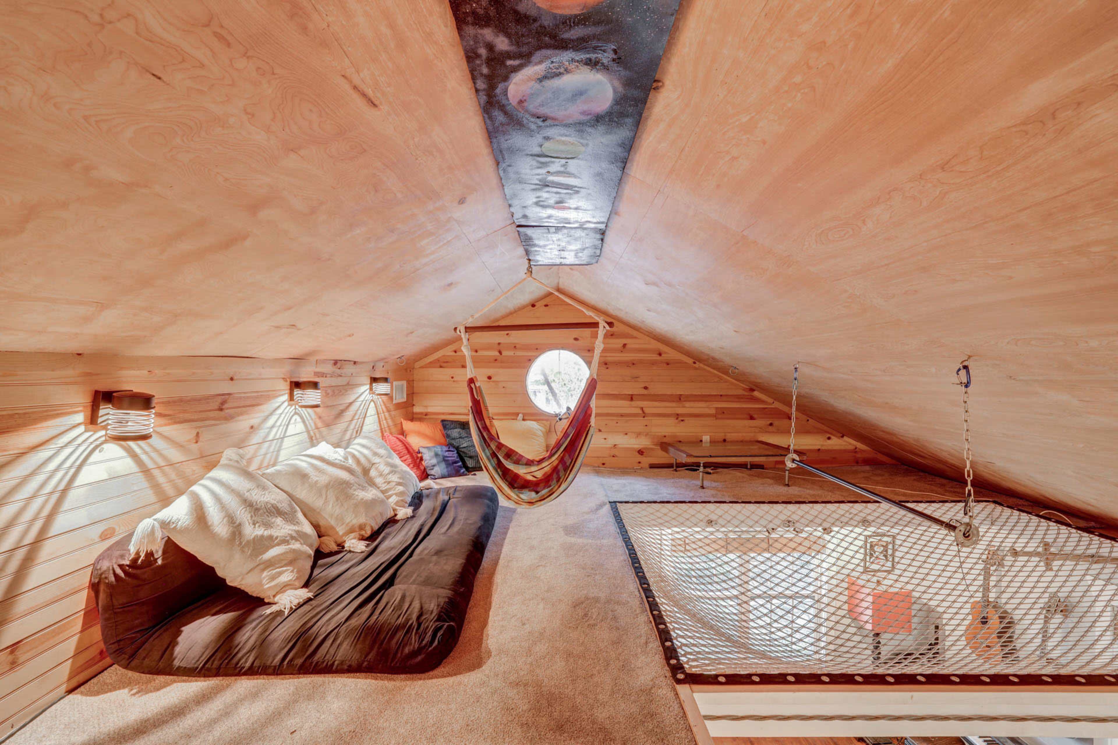A cozy attic space featuring wooden walls, a hammock, and a sleeping area with a black mattress.