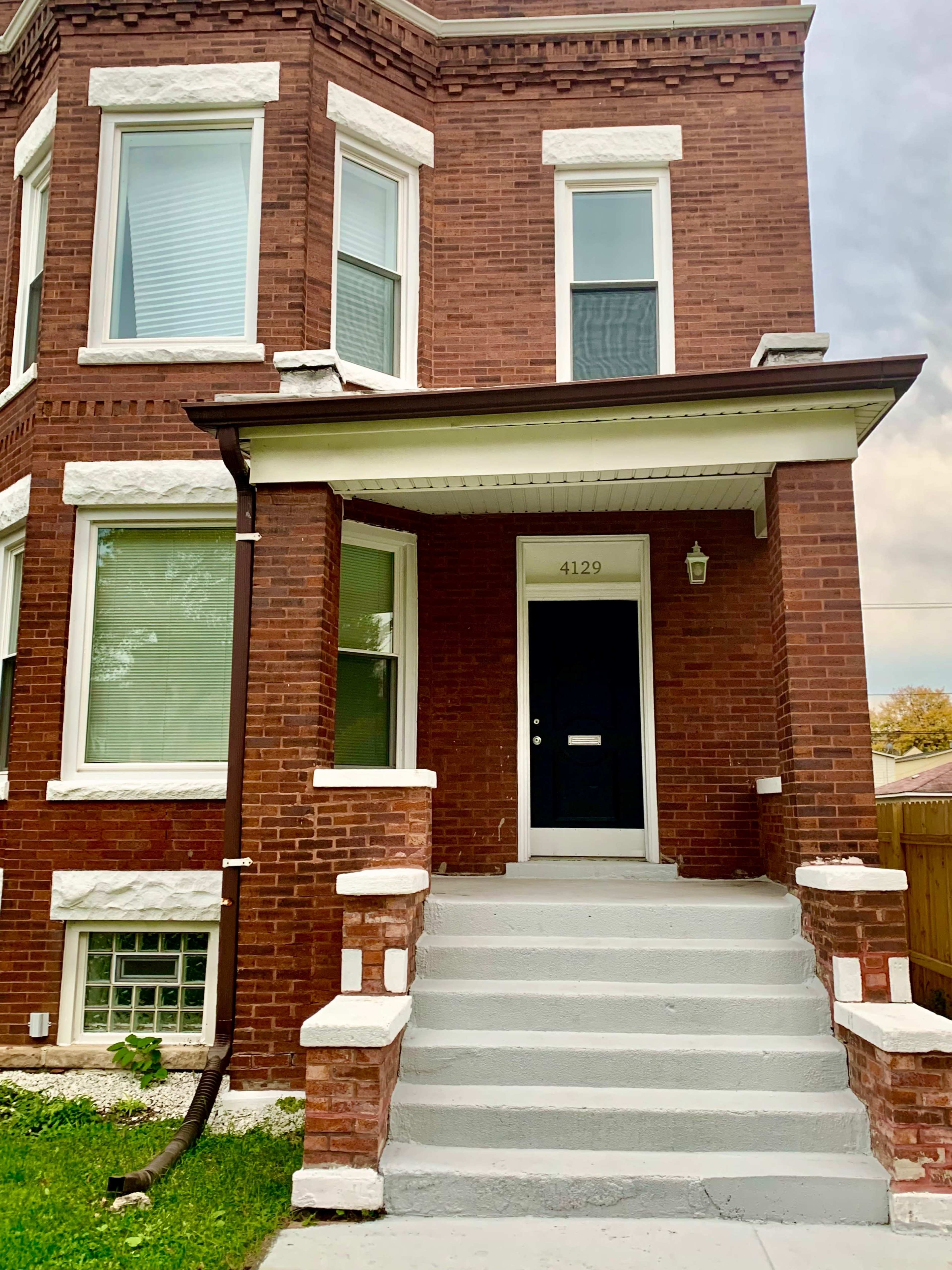 A brick building with a front porch, steps, and a black door labeled "4129."