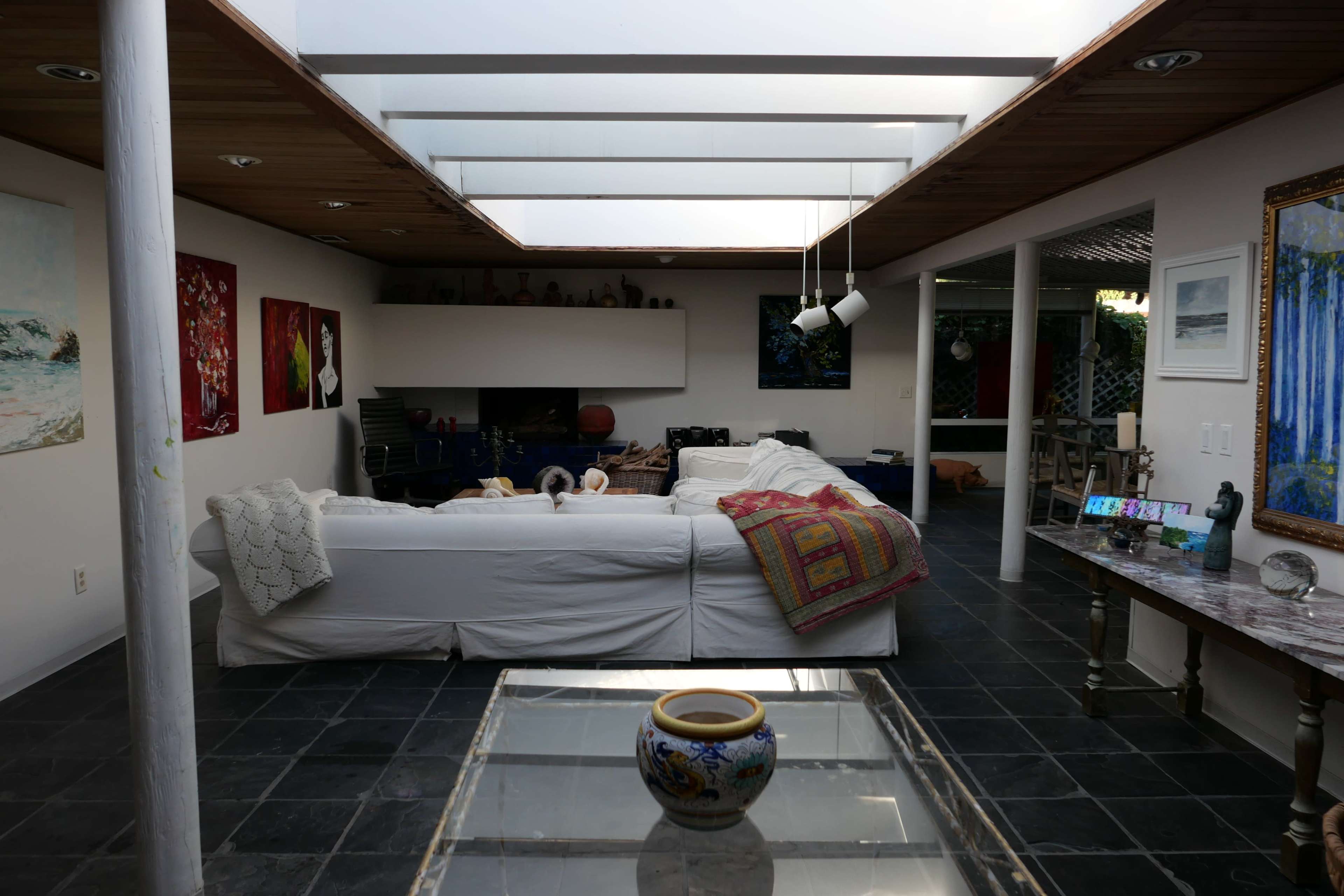 A spacious living area with a white couch, a glass coffee table, and art on the walls, illuminated by natural light through a skylight.