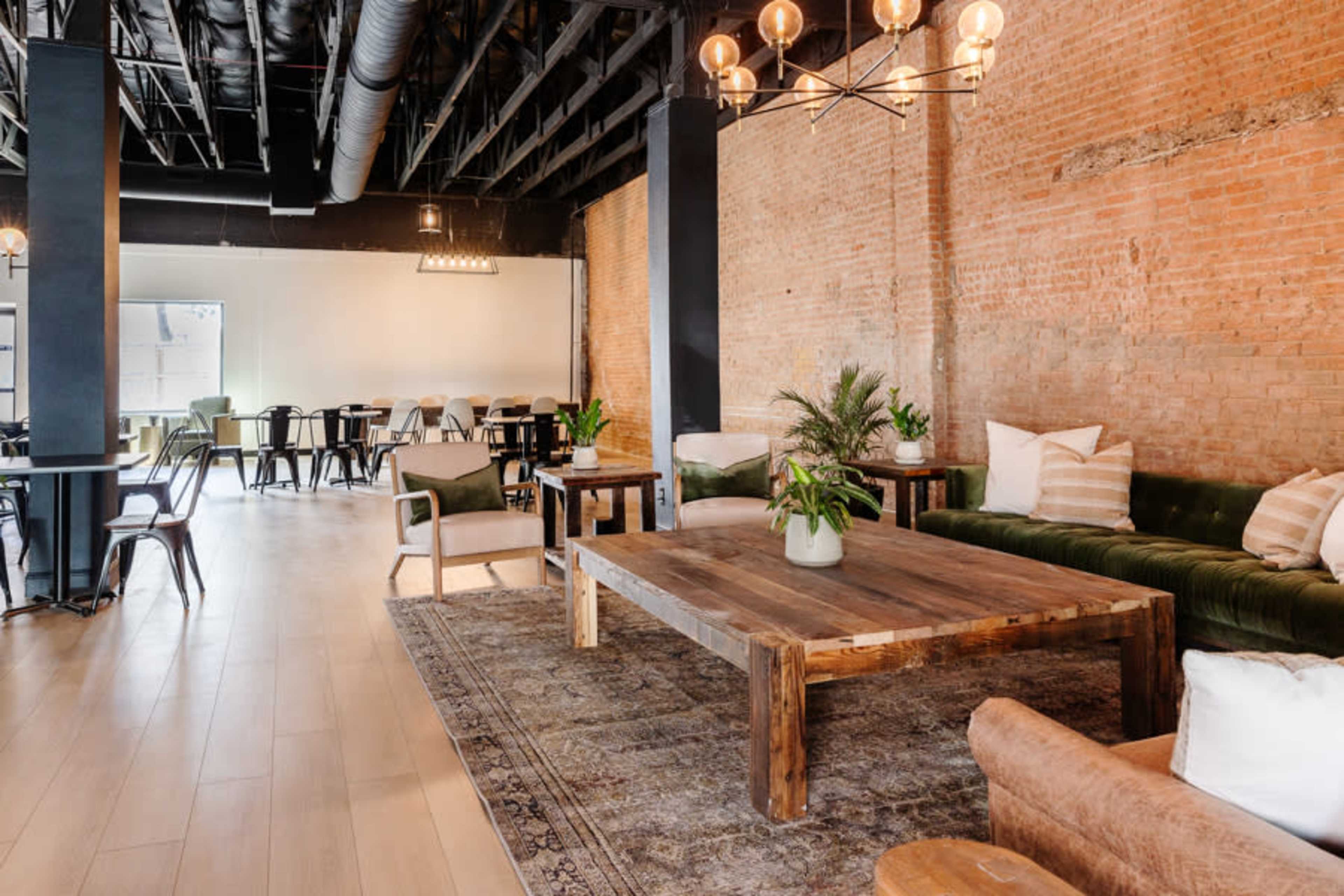 A spacious lounge area with exposed brick walls, a large wooden coffee table, and a mix of seating options, including couches and chairs.