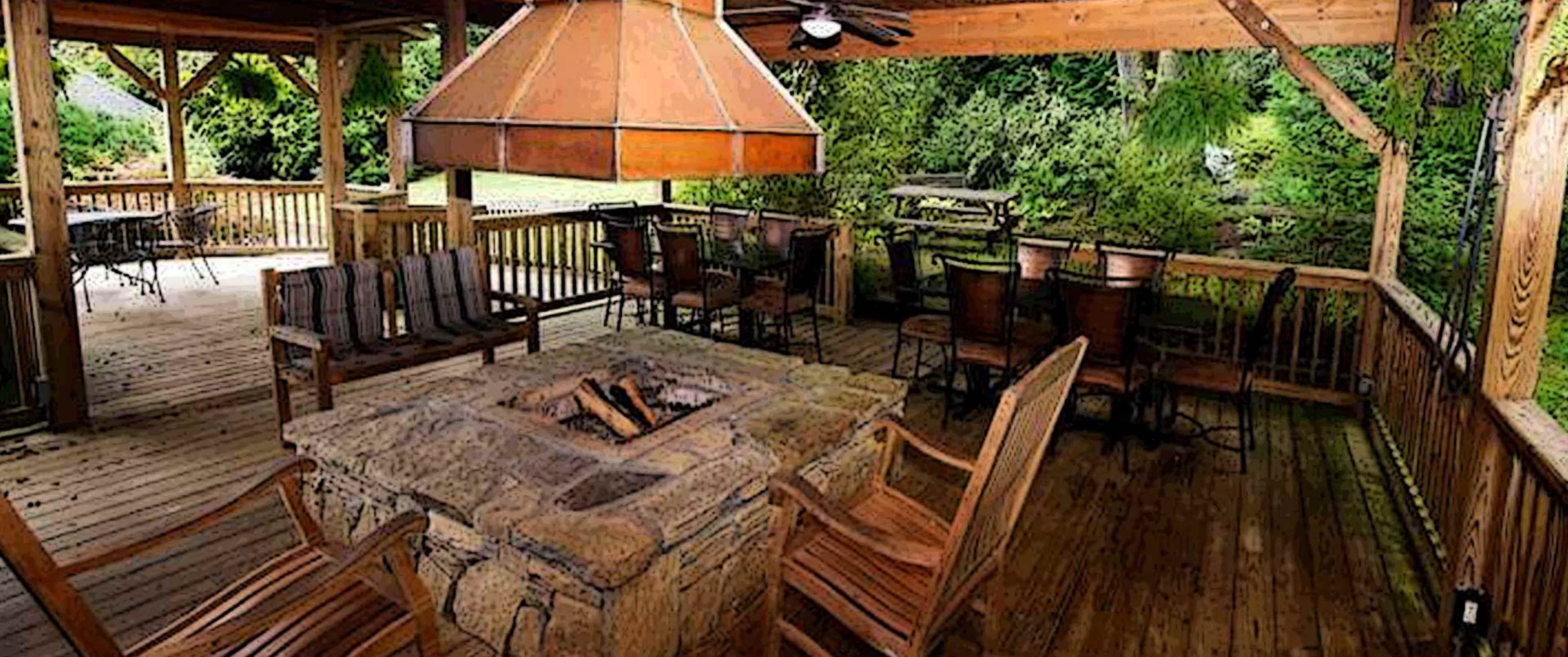 A wooden deck area with a stone fire pit at the center, surrounded by seating and a covered structure overhead.