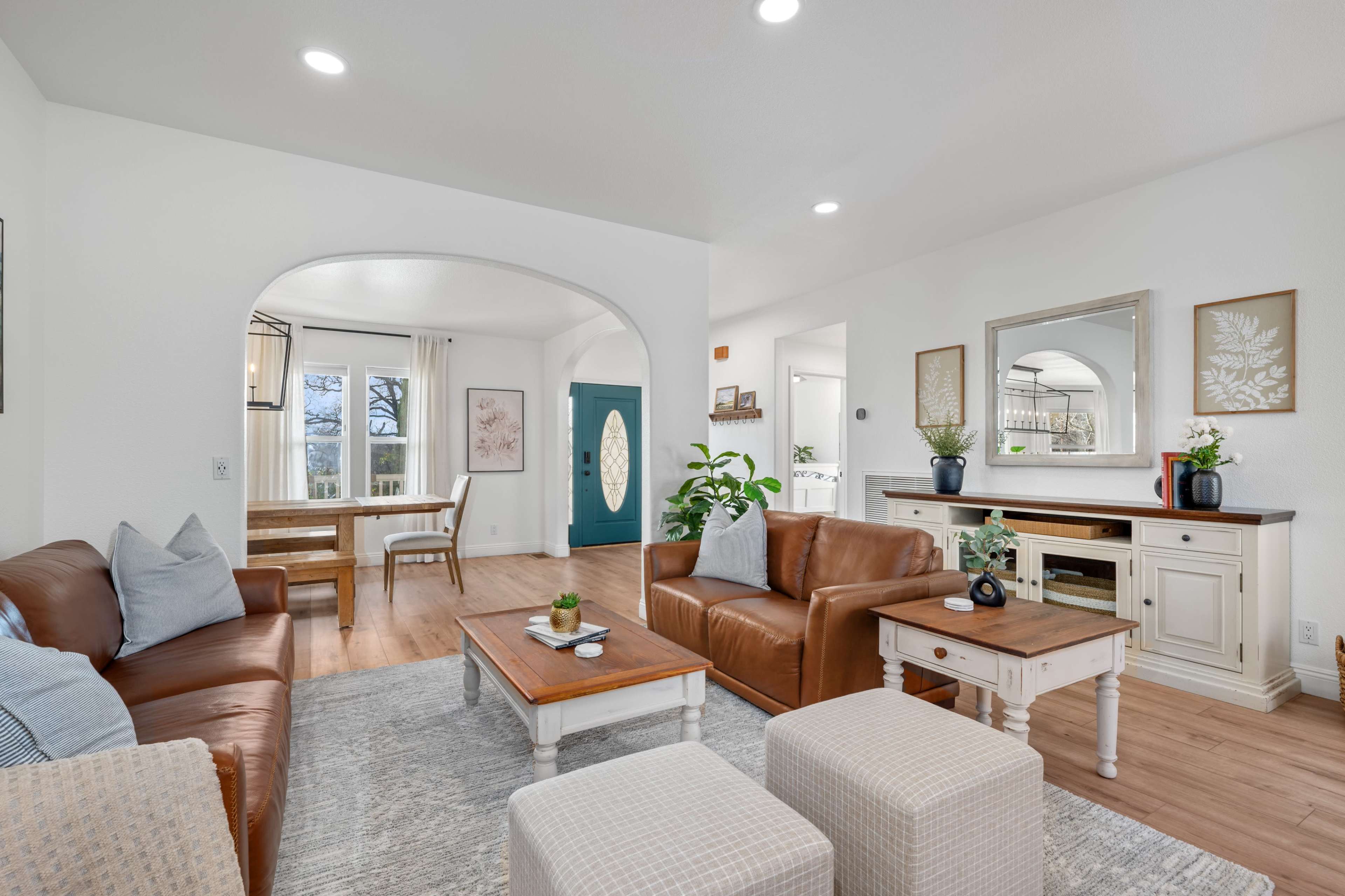 The image shows a bright living room featuring leather sofas, a wooden coffee table, and an archway leading to another area with a dining table.
