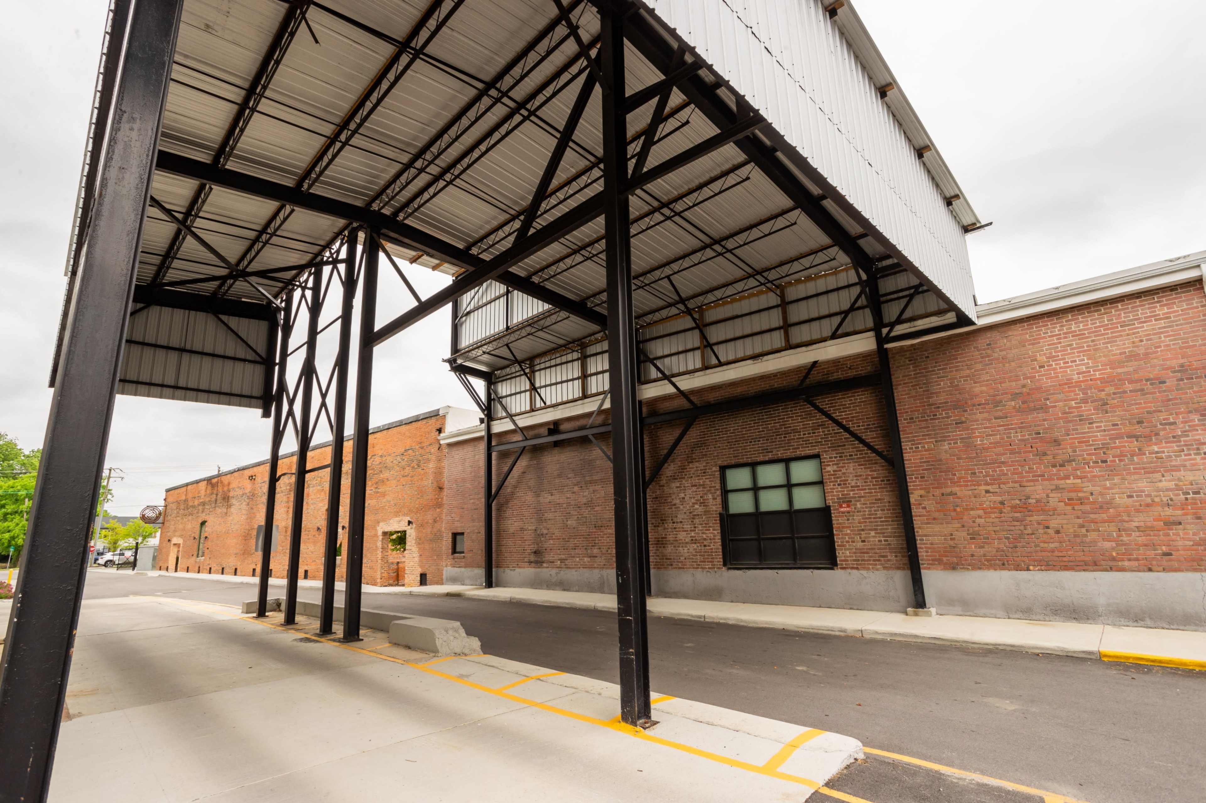 A covered walkway supported by metal beams alongside a brick building.
