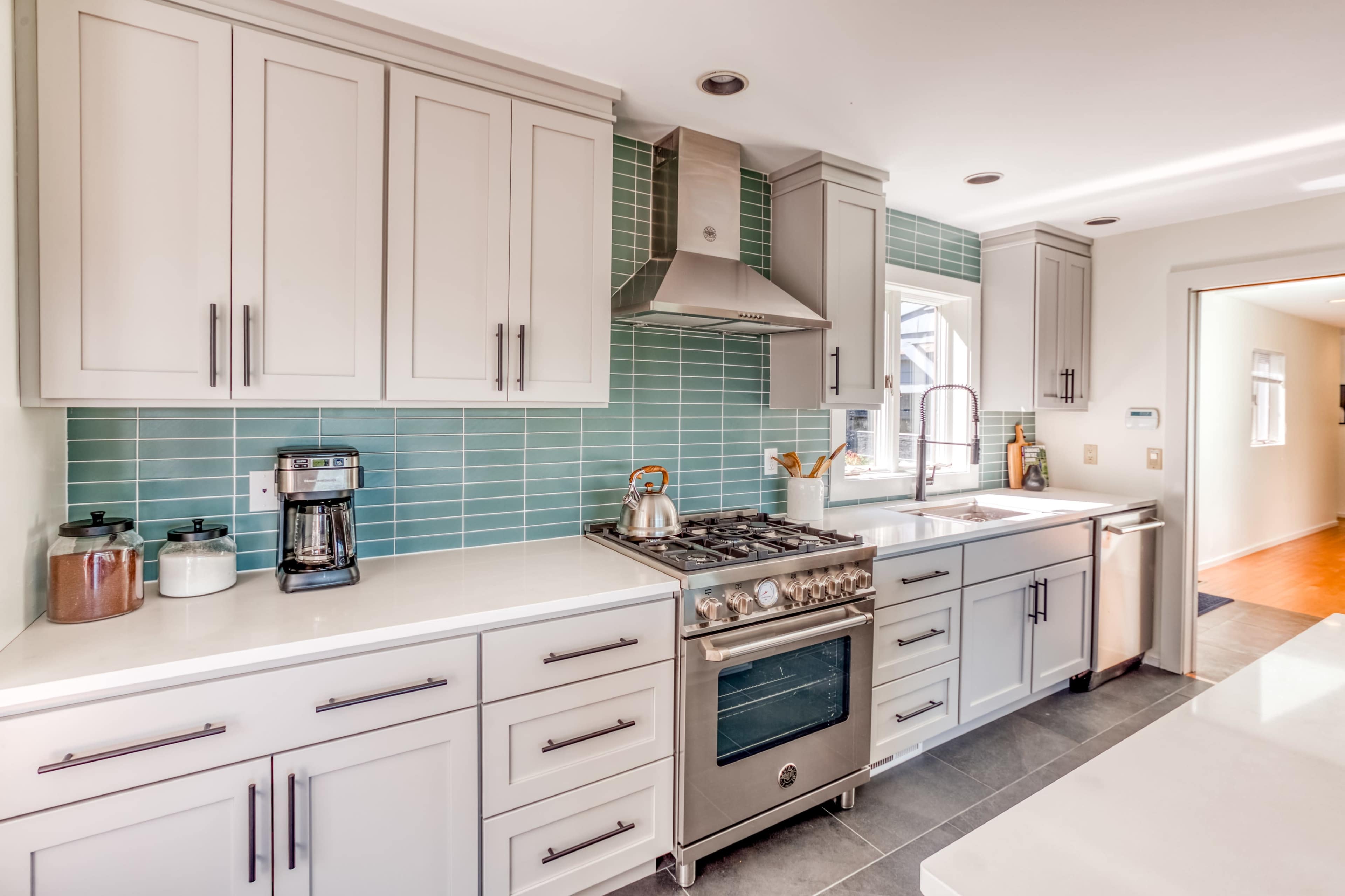 A modern kitchen features light gray cabinetry, a stainless steel range, and a turquoise tiled backsplash.