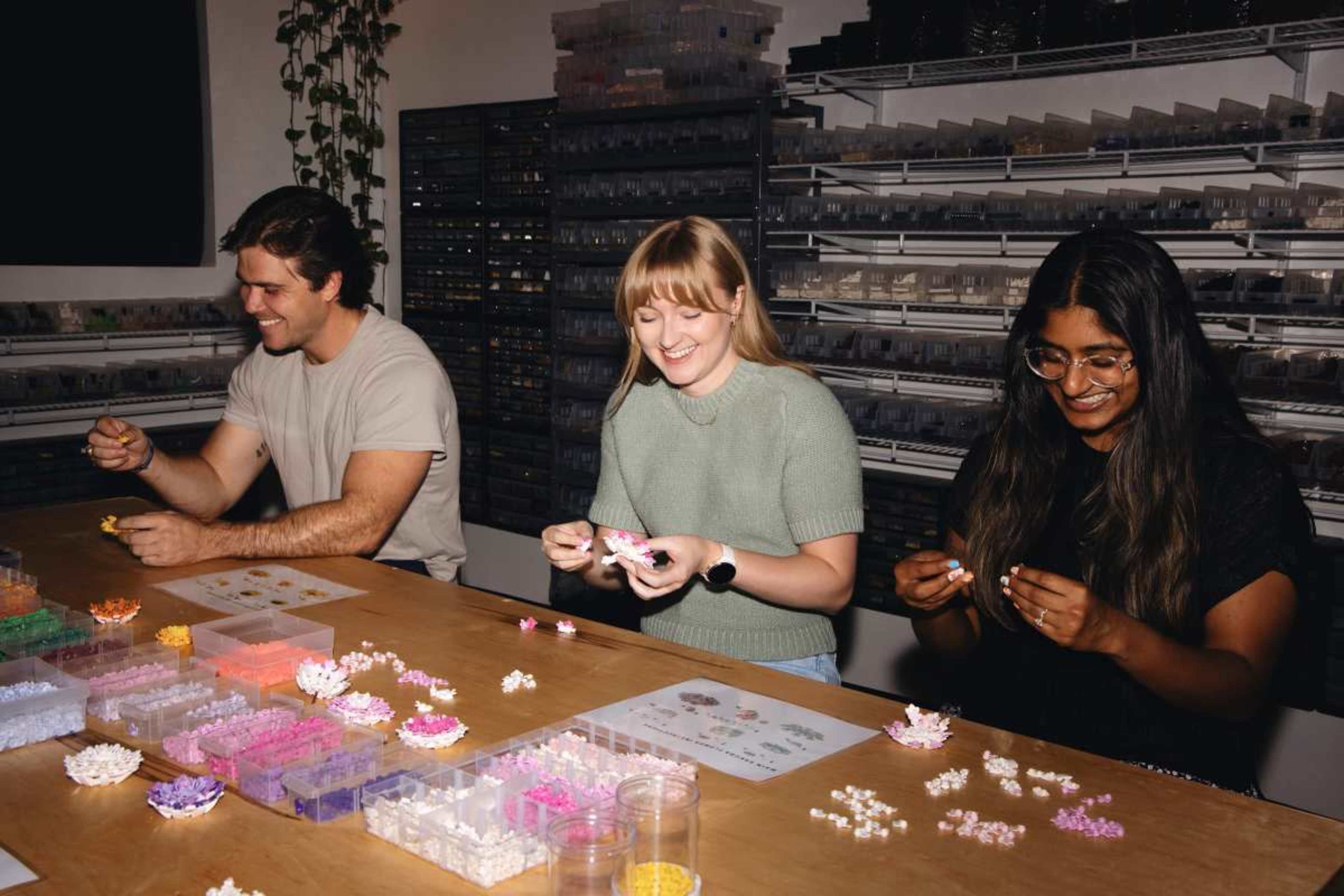 Three individuals are sitting at a table, engaged in a crafting activity with colorful materials spread out before them.