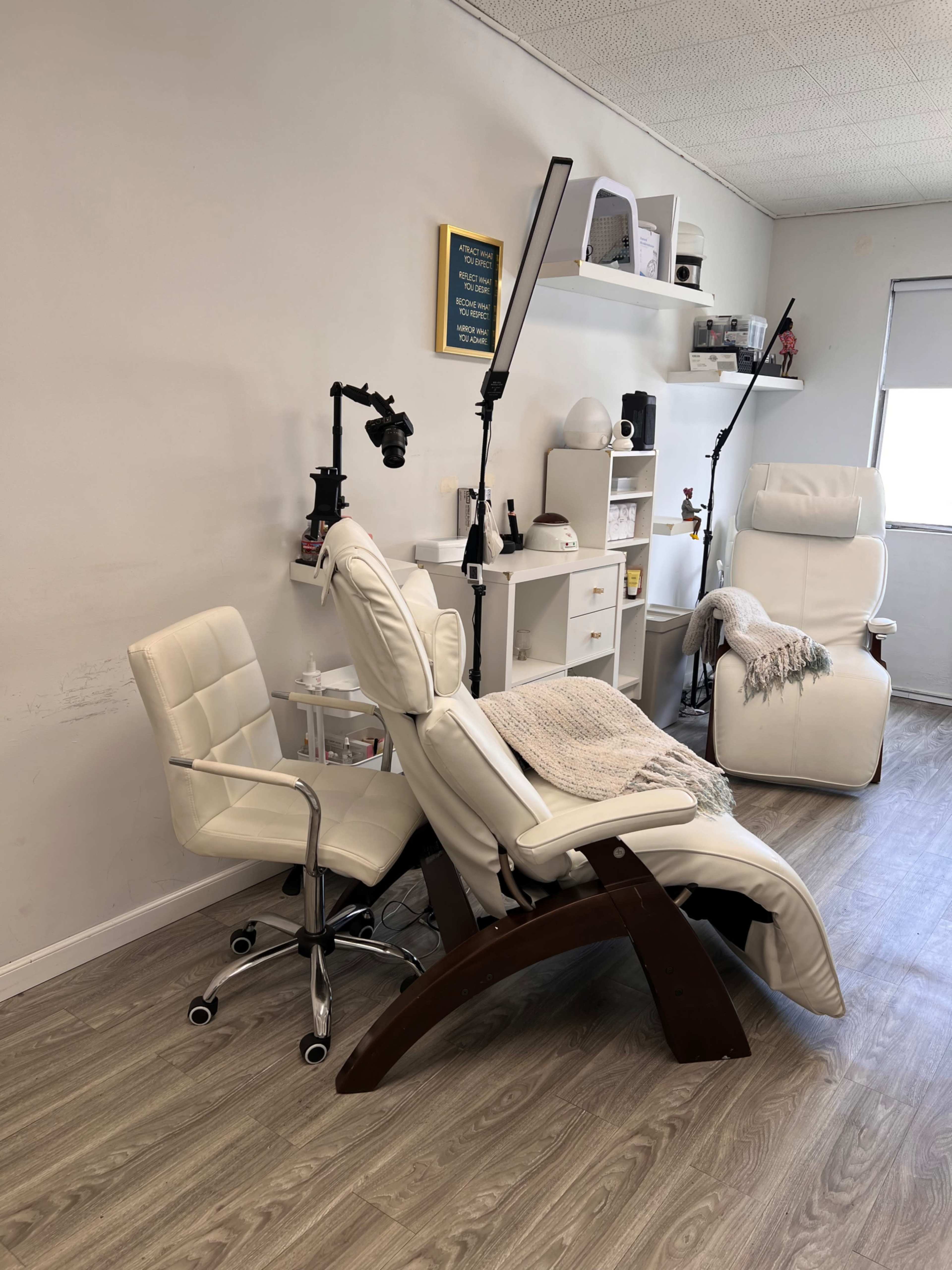 The image shows a well-lit salon interior featuring two white reclining chairs and several shelving units with various items and equipment.