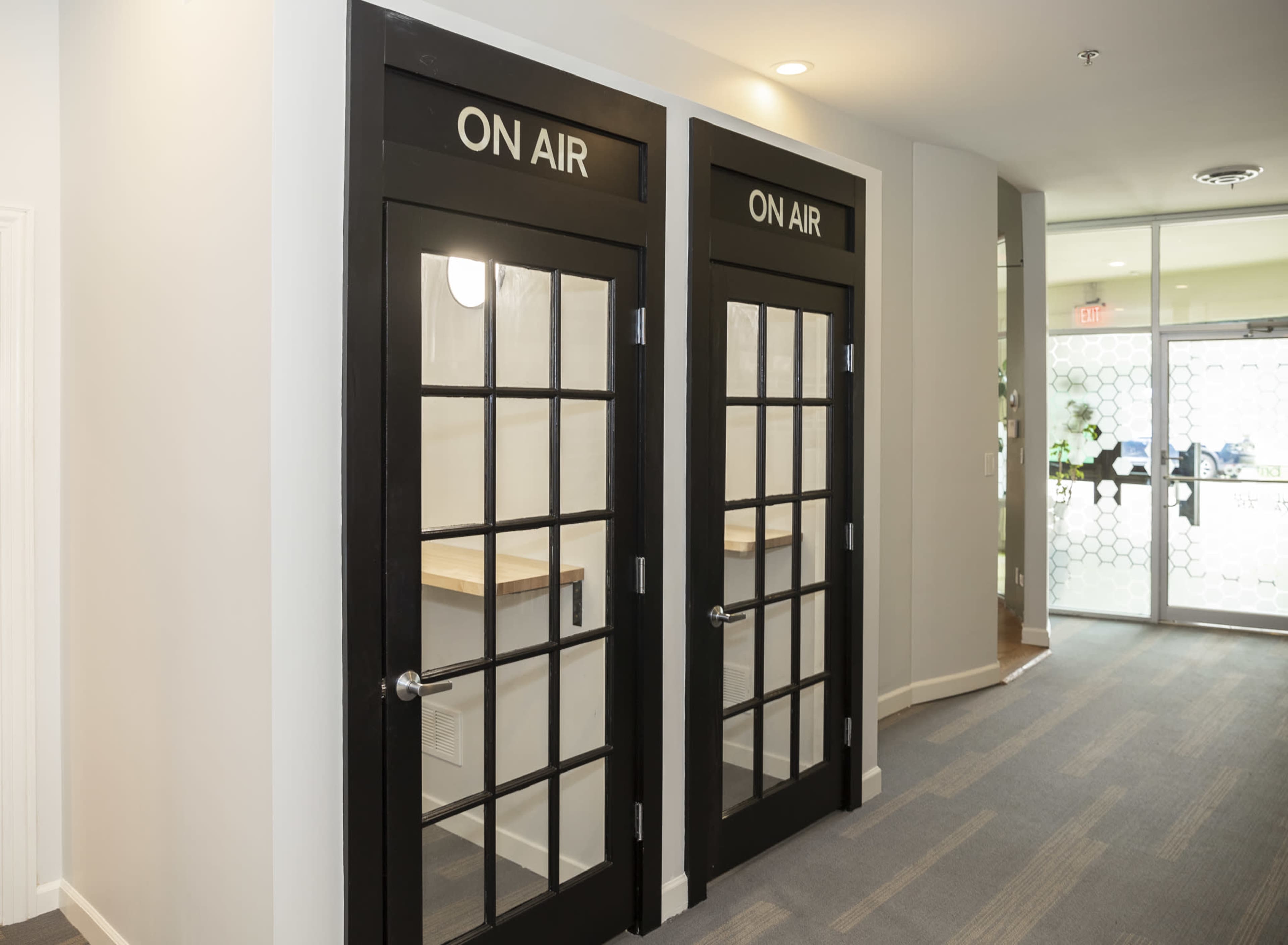 A hallway featuring two glass-paneled doors labeled "ON AIR" with a wooden counter visible inside each room.