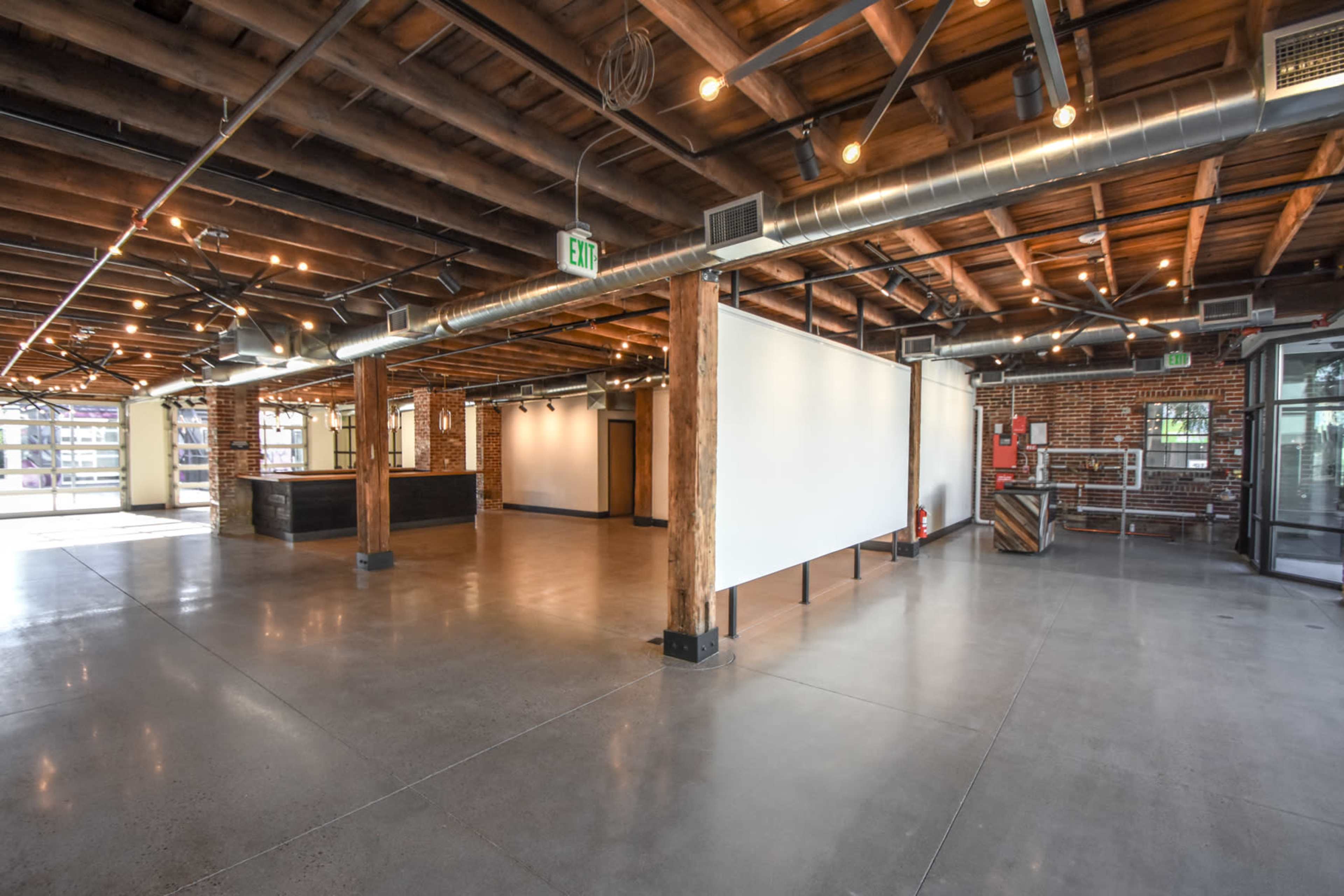 A spacious interior with exposed wooden beams, brick walls, polished concrete floors, and industrial-style pendant lighting.