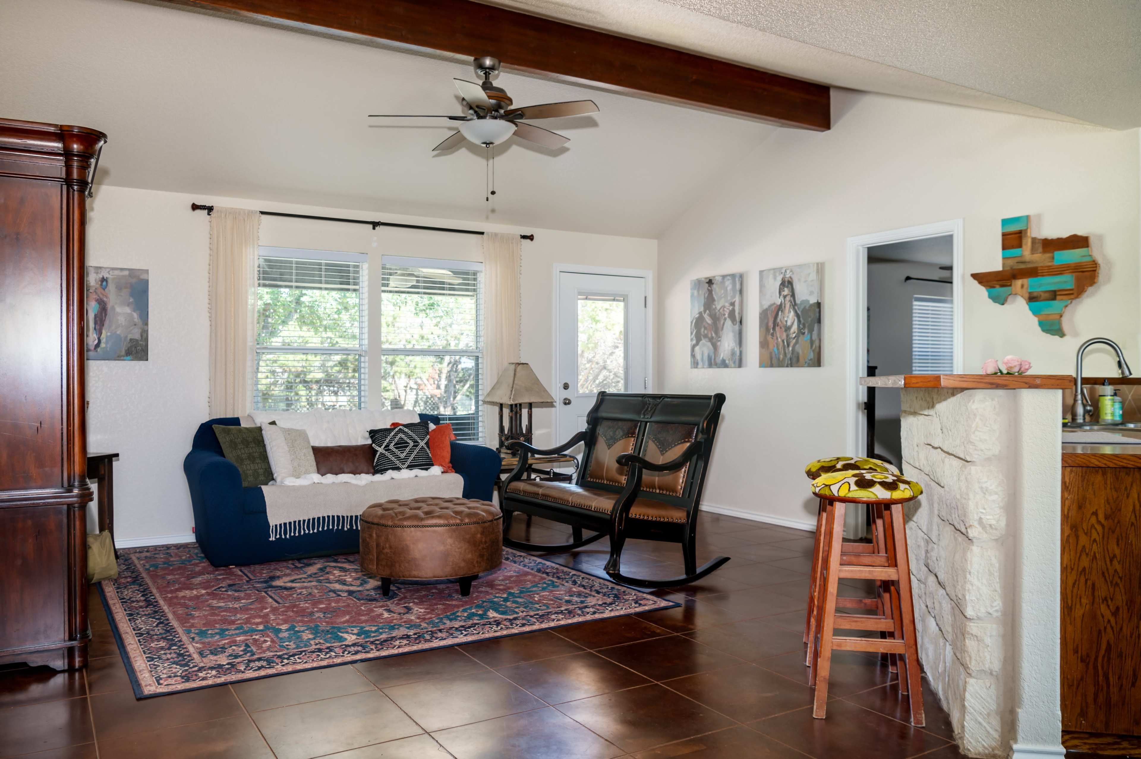 The living room features a blue couch, a brown ottoman, a rocking chair, and a small kitchenette with a stone bar.